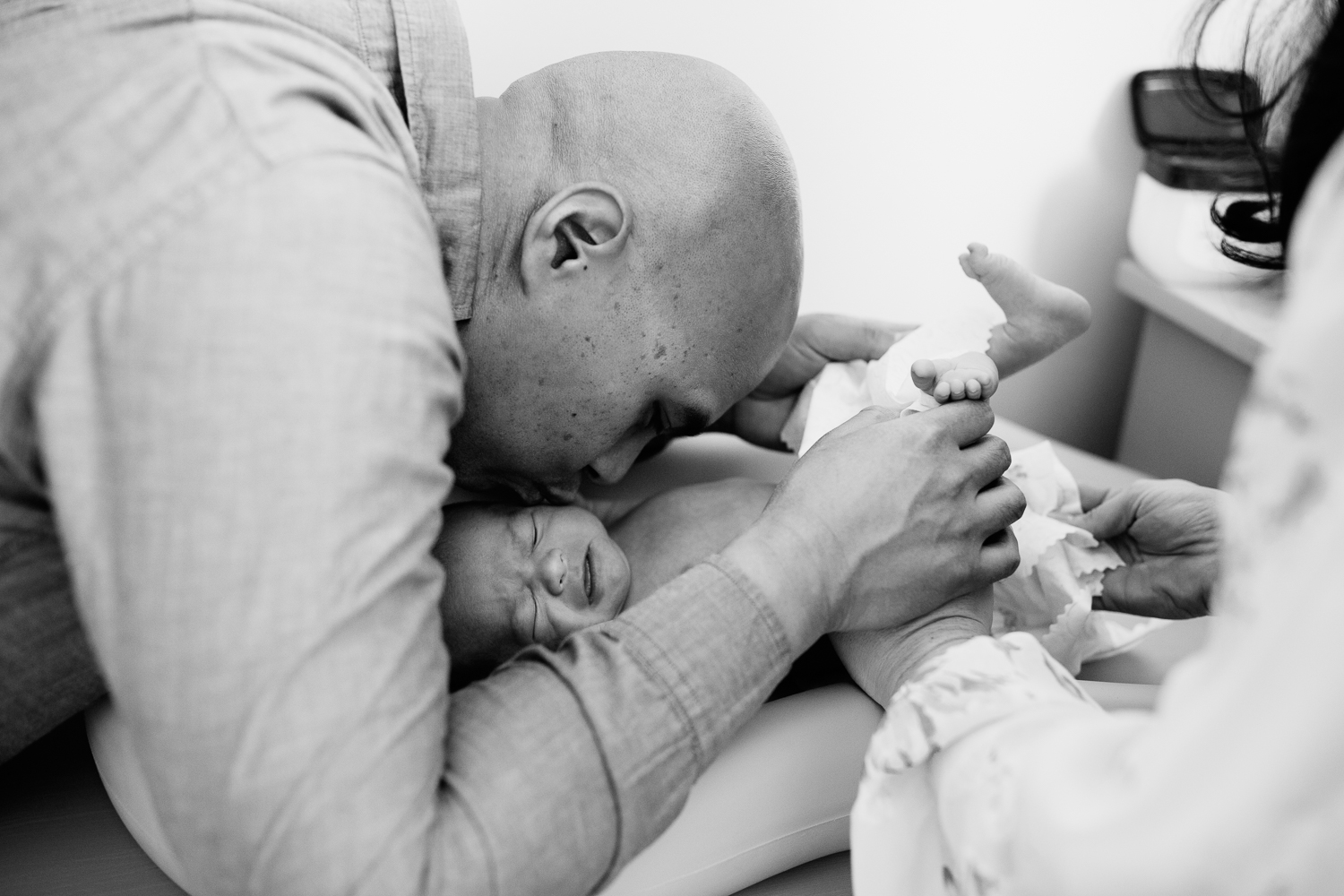new dad kissing 3 week old baby boy's cheek as he cries getting diaper changed by mom - Barrie In-Home Photography