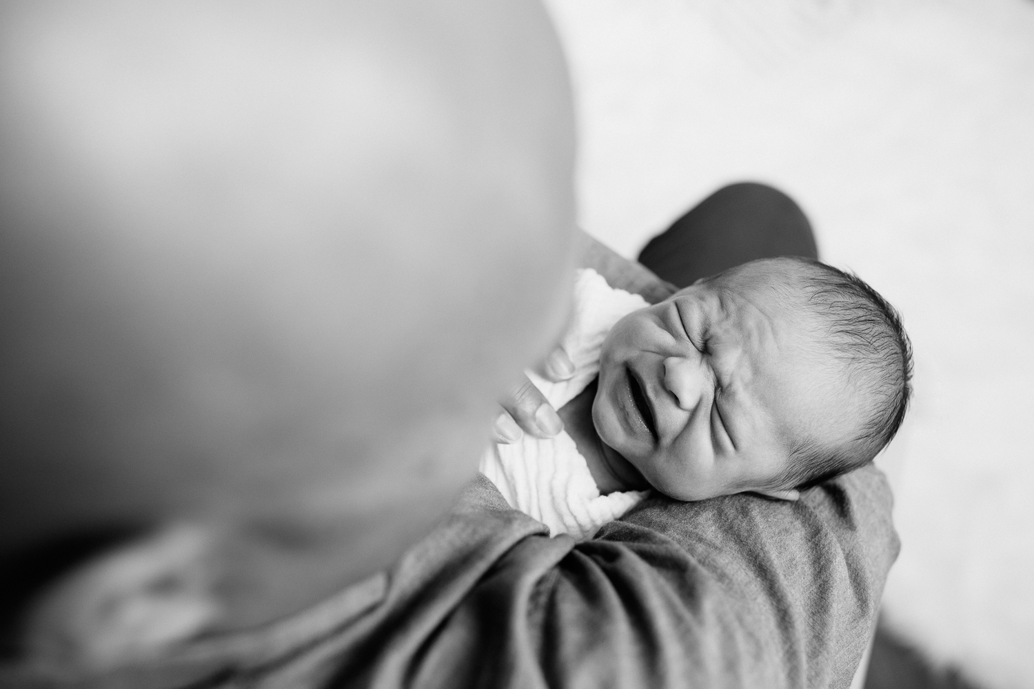 3 week old baby boy in swaddle in dad's arms, eyes closed, scowling - Markham Lifestyle Photos