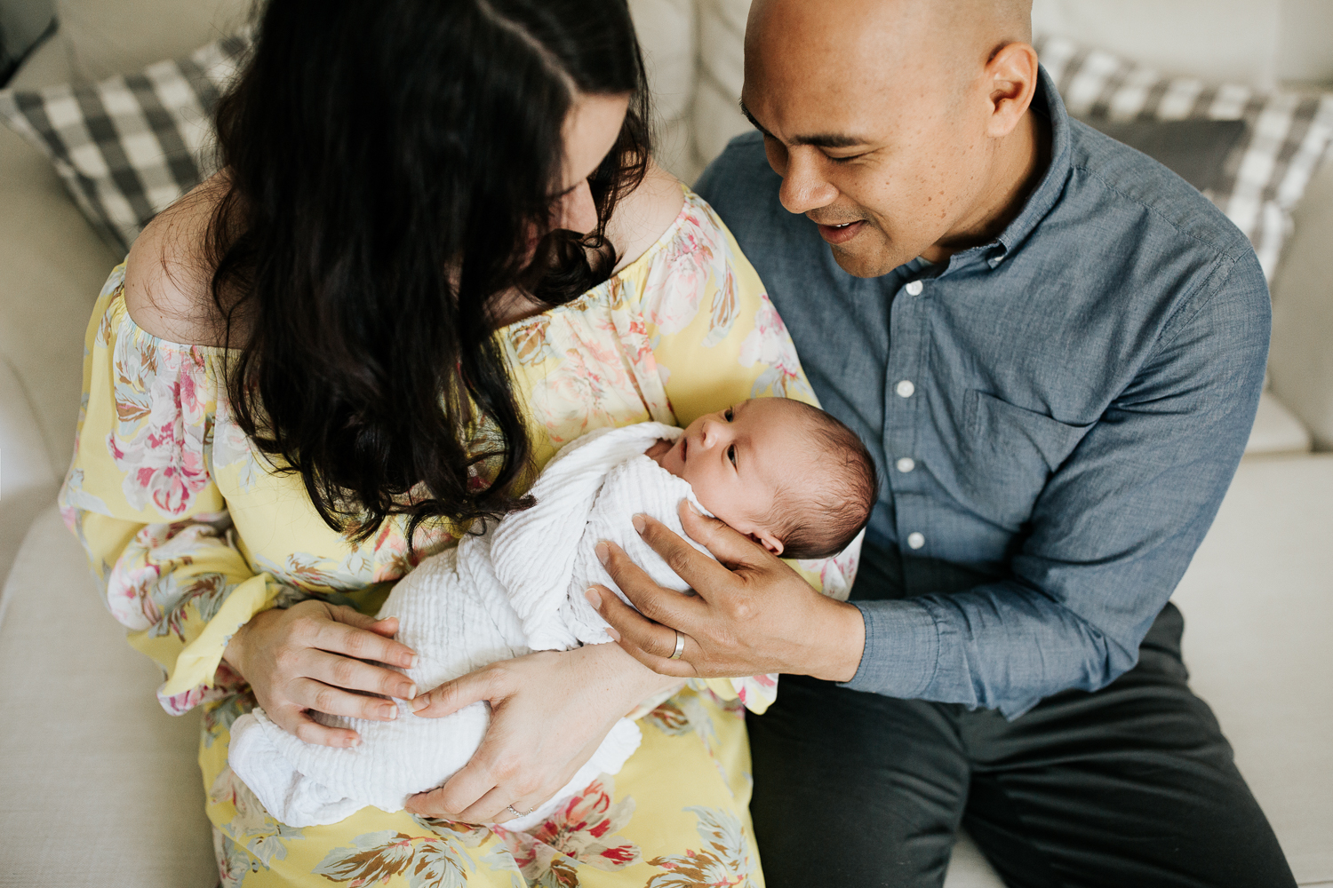 new parents sitting on couch, 3 week old baby boy in mother's arms, dad's hand on son - Markham Lifestyle Photography