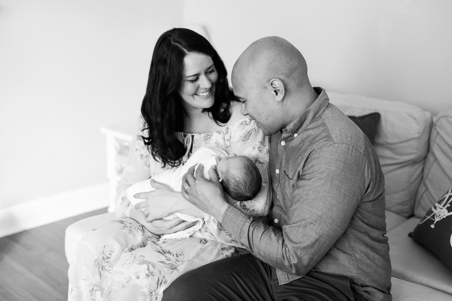 new parents sitting on couch, 3 week old baby boy in mother's arms as she looking up and smiles at husband, dad looking at son - GTA Lifestyle Photos
