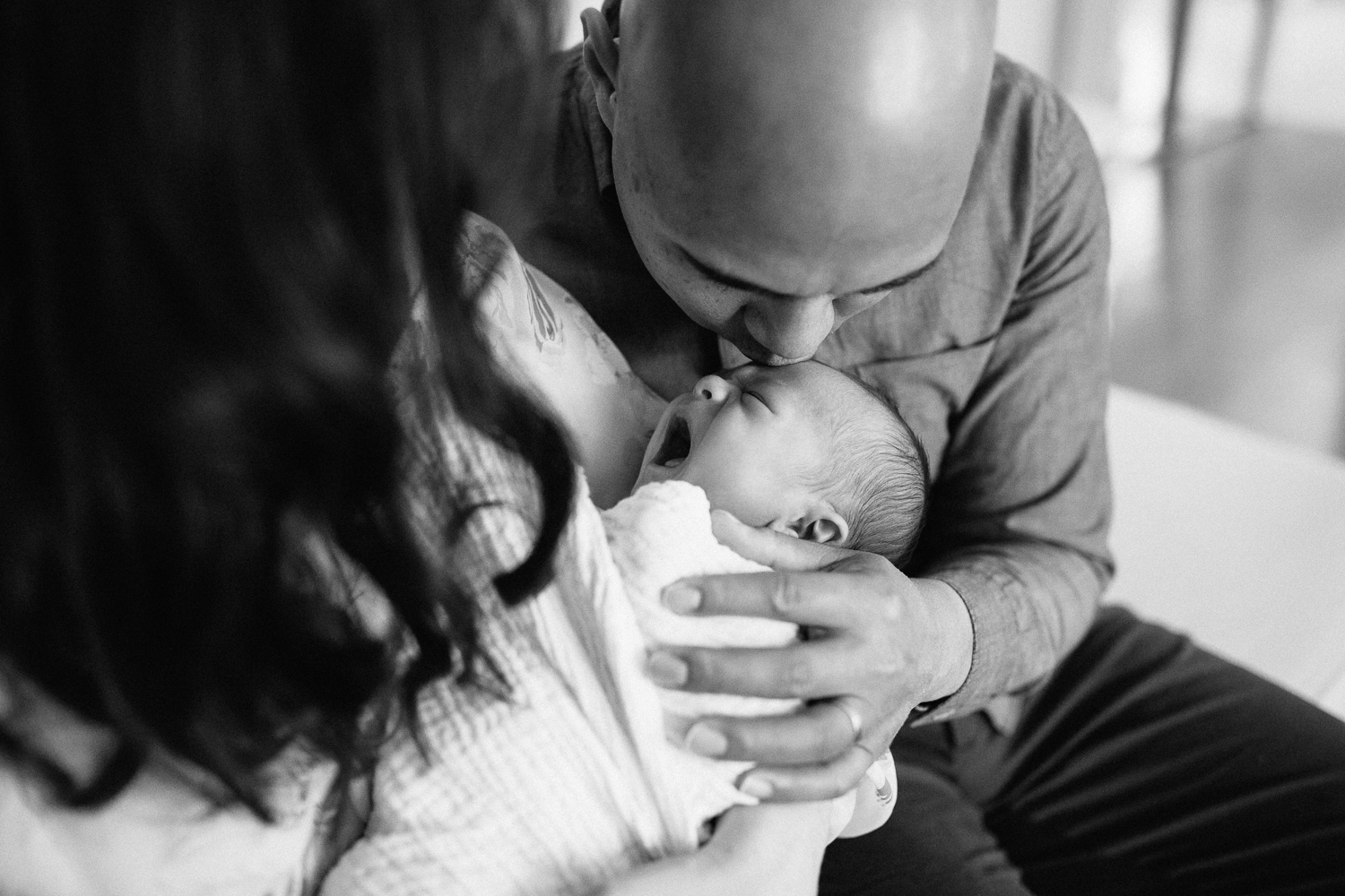 new parents sitting on couch, 3 week old baby boy in mother's arms, father kissing son on forehead - Stouffville Lifestyle Photography