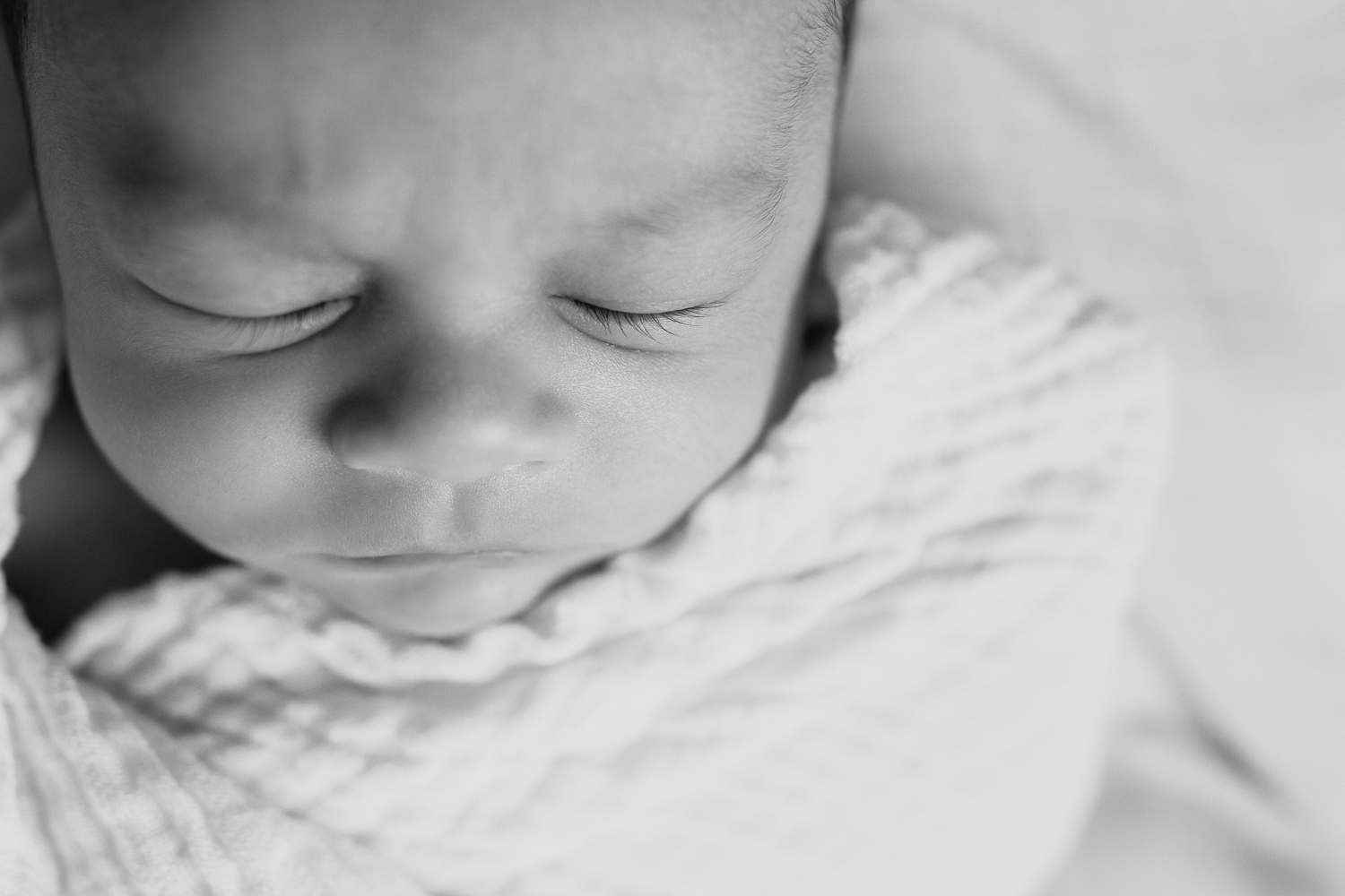 3 week old baby boy with dark hair sleeping wrapped in white swaddle, black and white portrait - Barrie In-Home Photography
