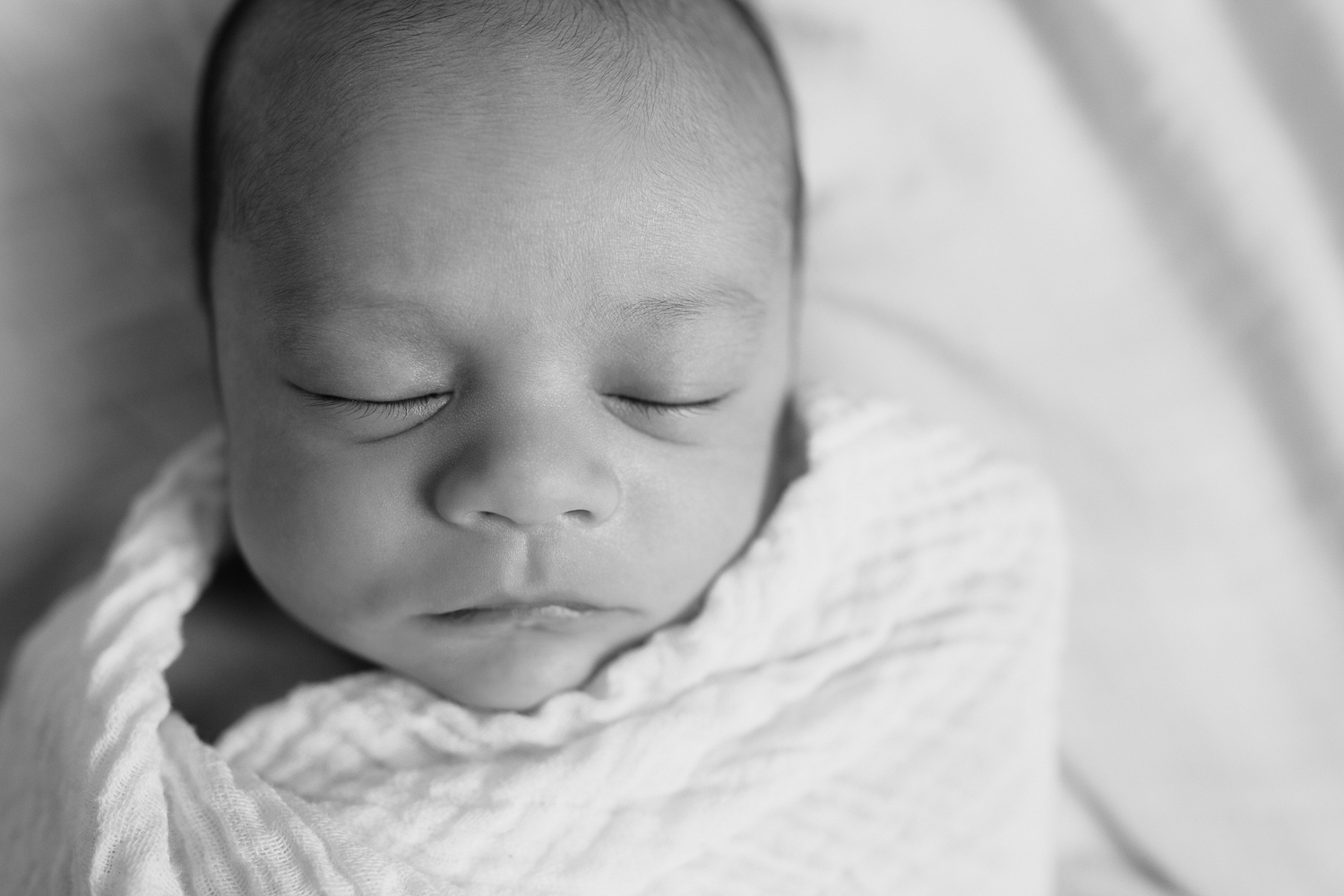 3 week old baby boy with dark hair sleeping wrapped in white swaddle, black and white portrait - Newmarket In-Home Photos