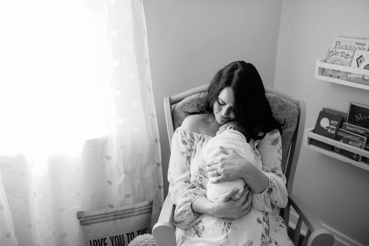 new mother sitting in nursery rocker snuggling 3 week old baby boy on her chest, mom's chin resting on son's head - Markham Lifestyle Photography