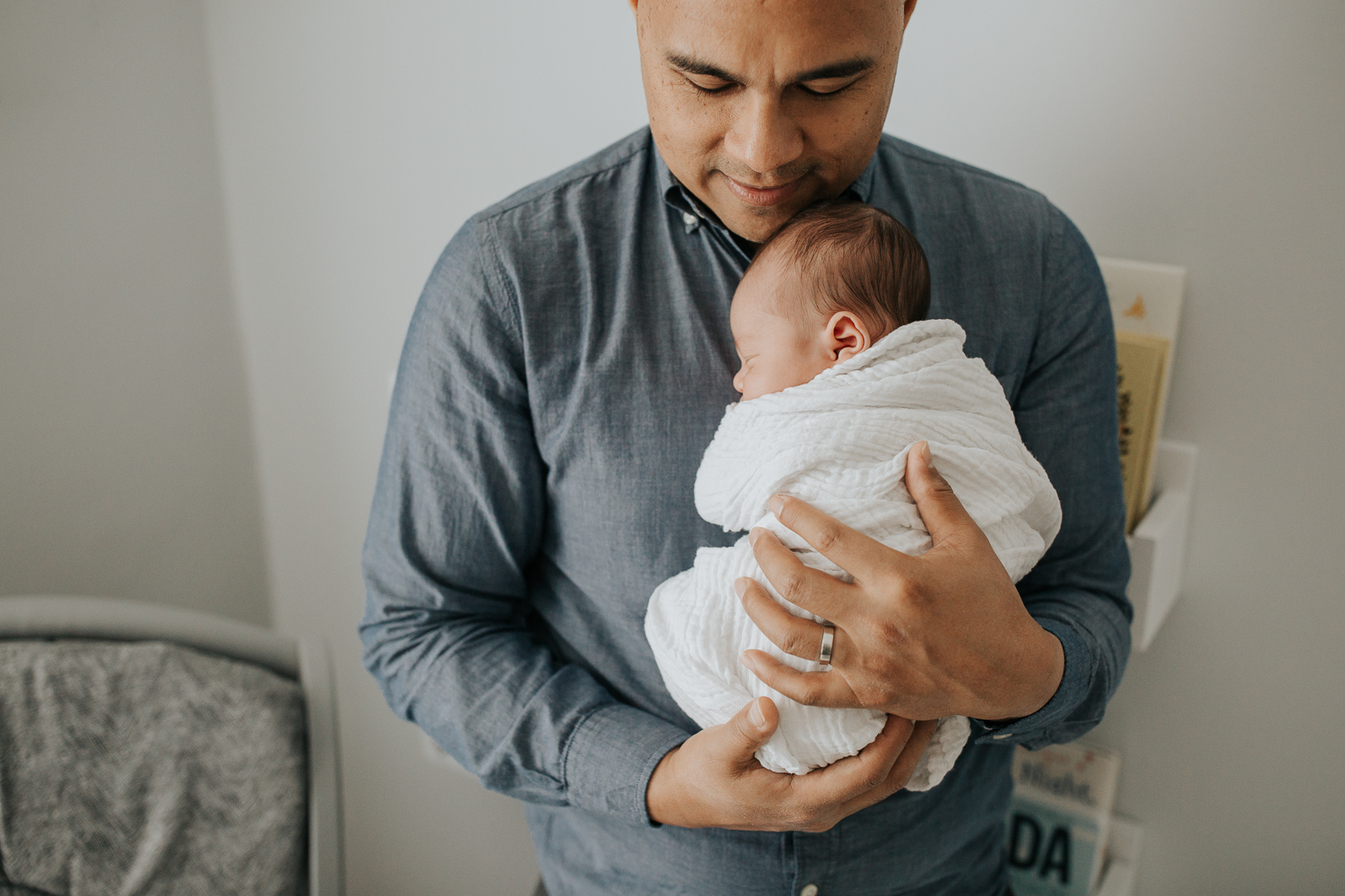 new father standing in nursery snuggling 3 week old baby boy sleeping in white swaddle, dad looking down at son - Stouffville In-Home Photography