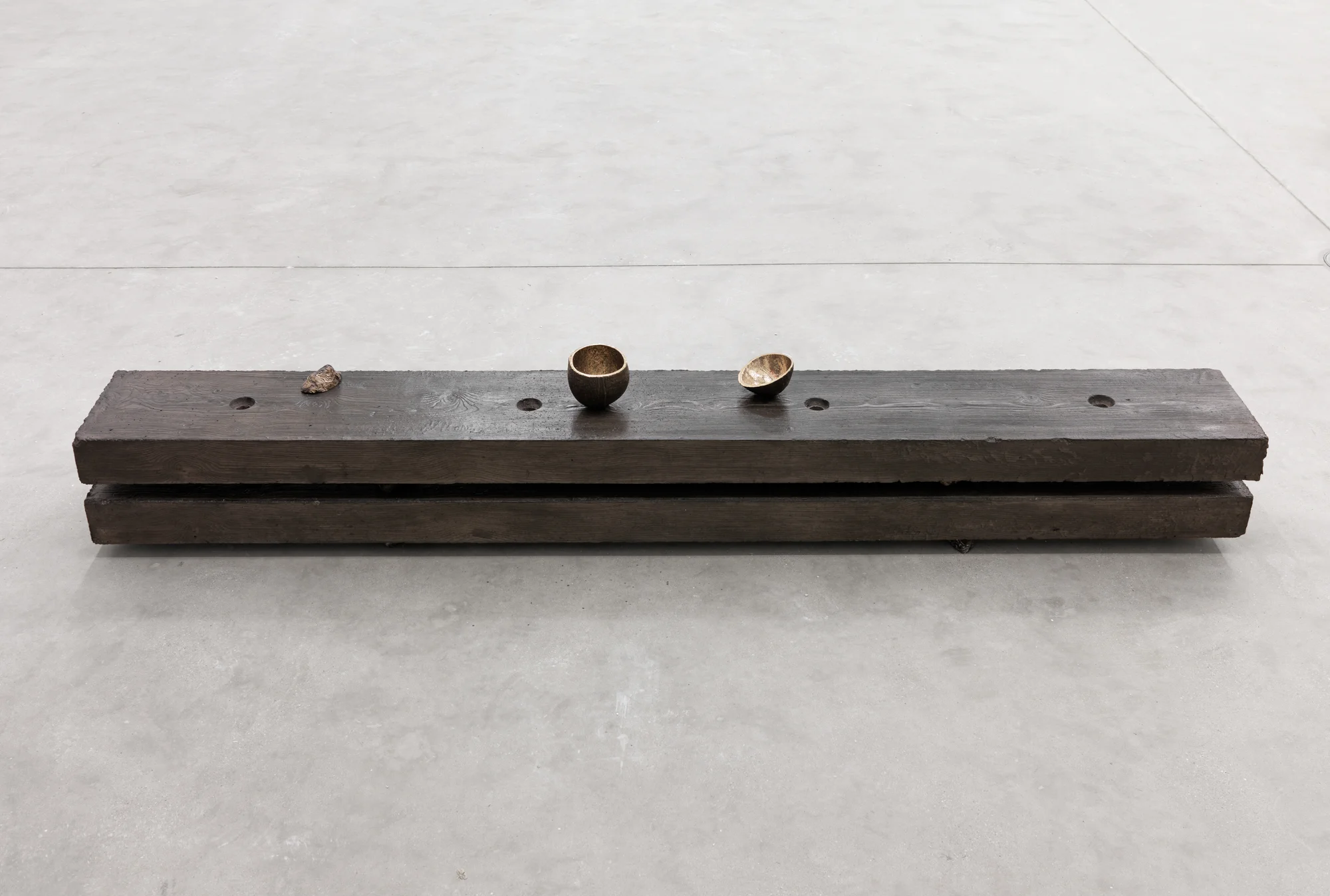 Misery Farm: Arrangement Four , 2012 Concrete, Hepworth brown concrete colouring, Carnauba wax, lanolin, carbon black 650 x 250 x 2000 mm Details of individual works within arrangement: This is a love story, and we are the lovers , 2015 Bronze, two parts 150 x 150 x 200 mm (bronze coconut) I found the child not far from the house lying face down by the edge of the frozen stream , 2015 Stoneware, manganese dioxide 30 x 40 x 50mm (small oyster shell)