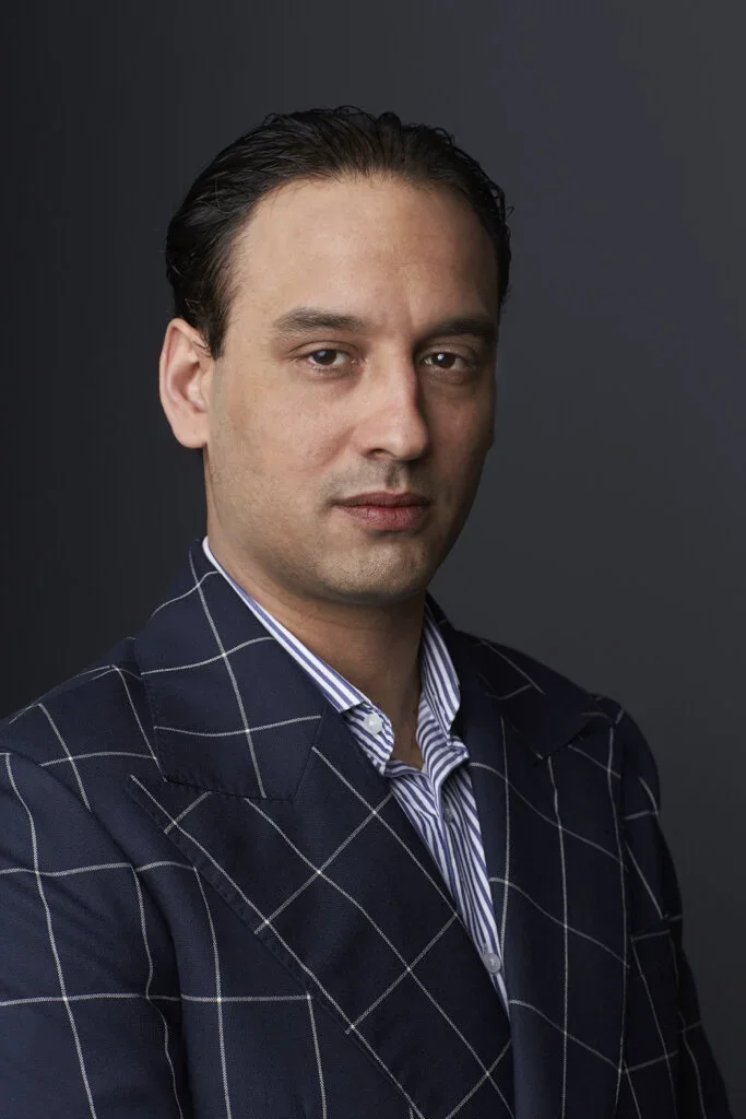 Portret van Jean-Paul Samson, oprichter en kleermaker van De Oost Bespoke Academy, in een donkerblauw geruit jasje op maat met gestreept overhemd