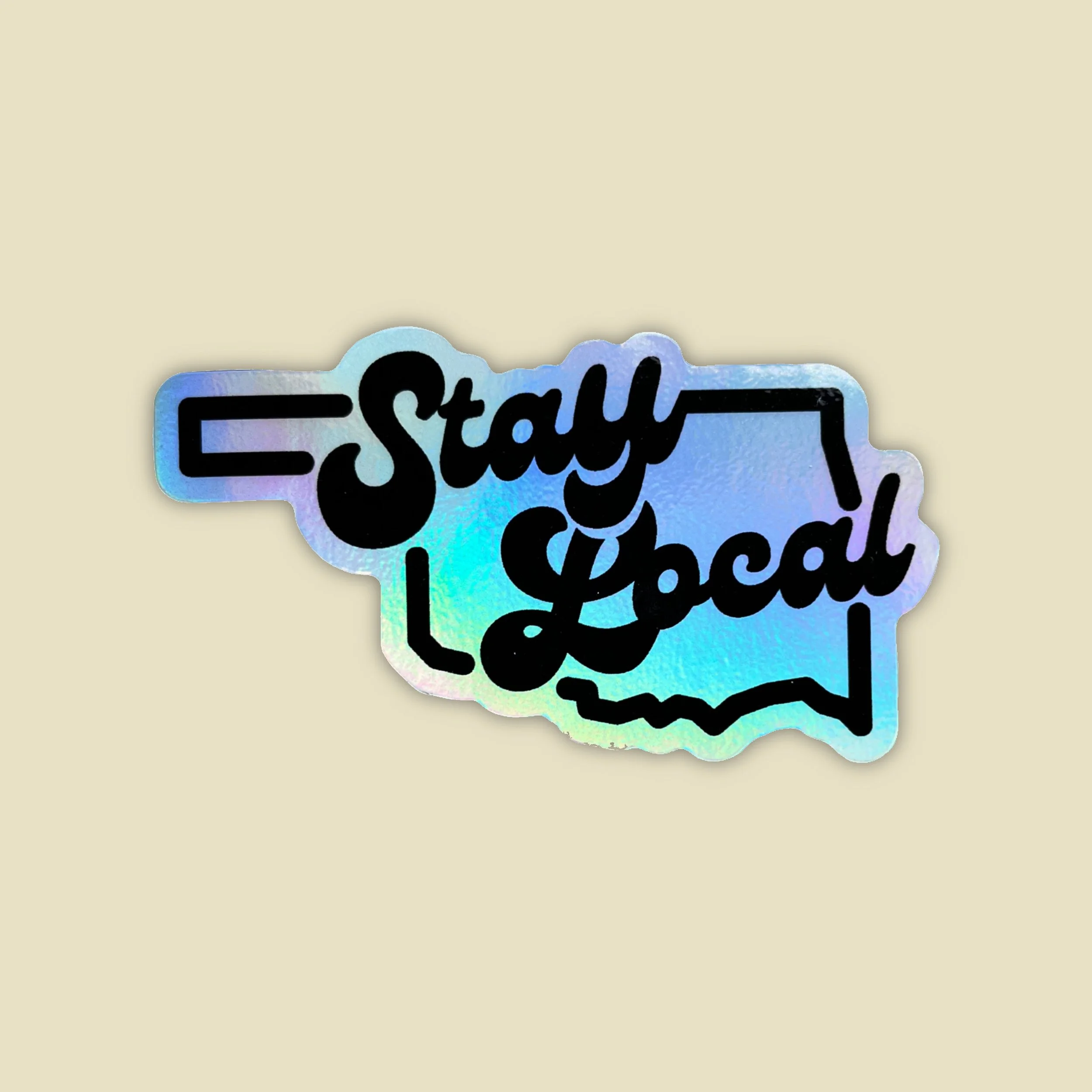 a holographic sticker in the shape of oklahoma that says  "stay local"