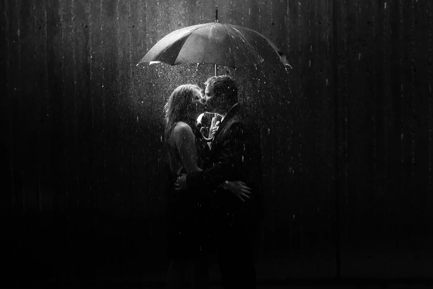 Bride and groom kissing under an umbrella in the rain