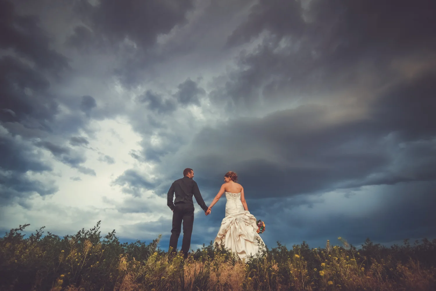 Bride and groom standing on hilltop with clouds in background