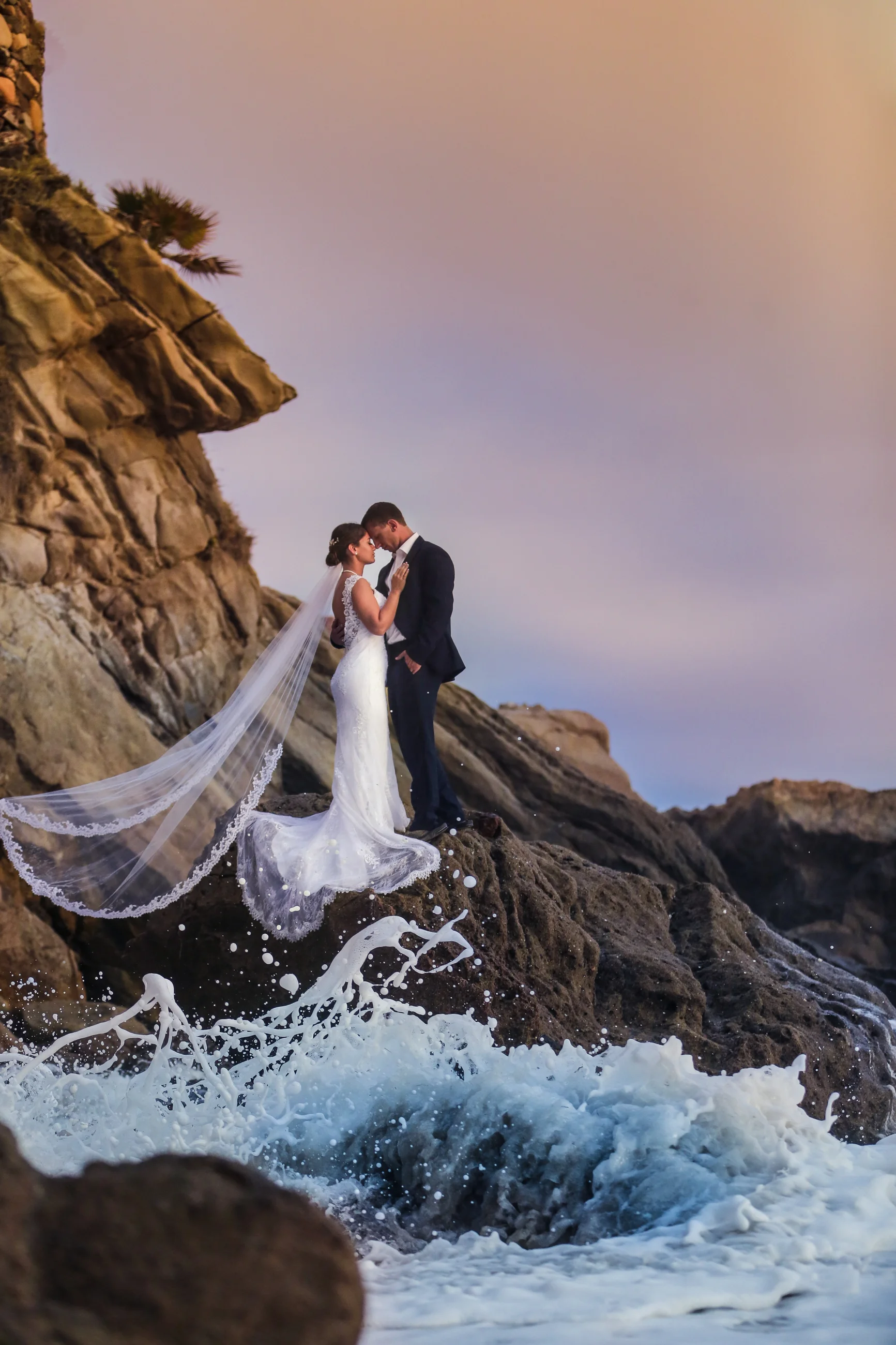 California Bride and groom on rocks with ocean waves crashing around