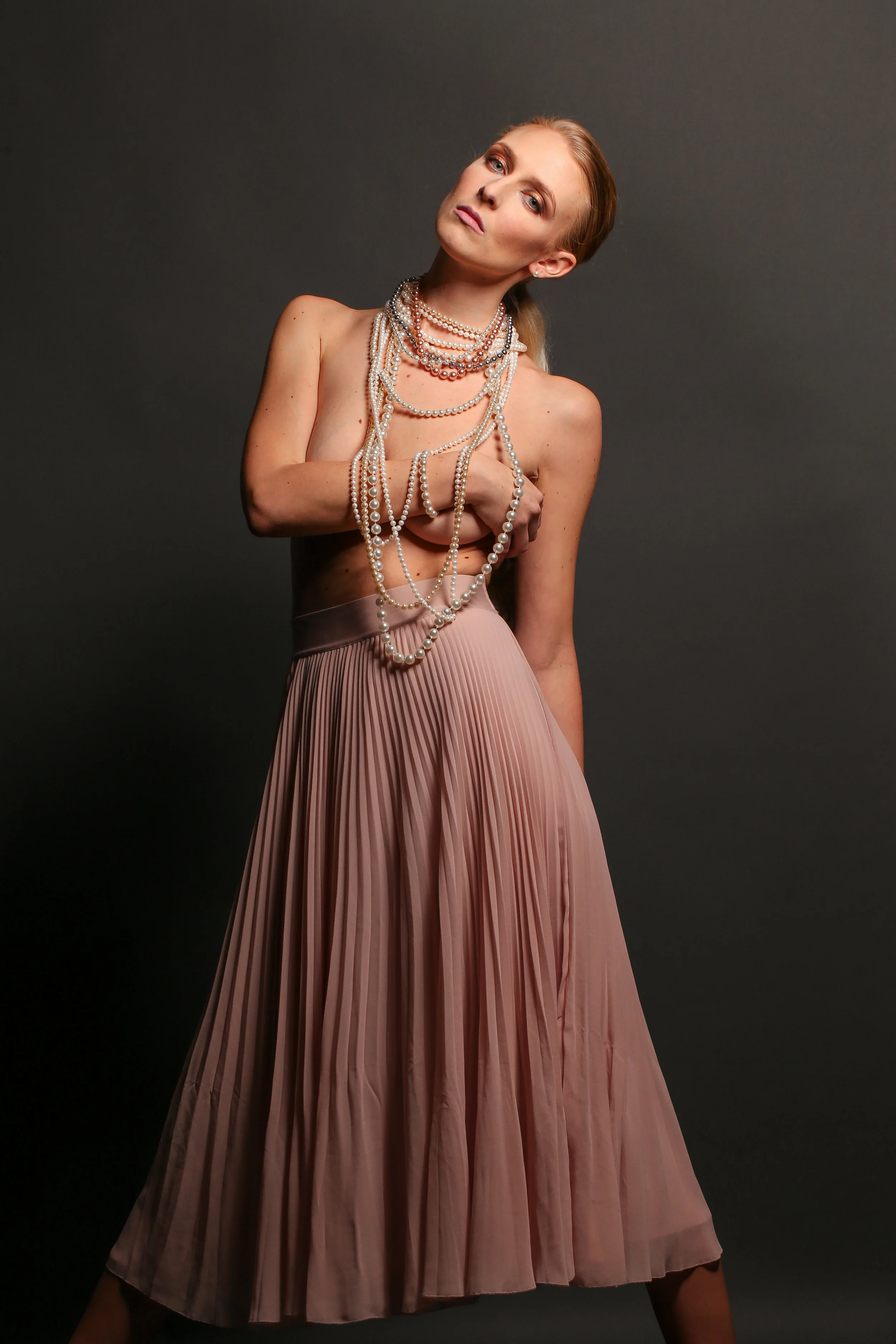 Fashion model in editorial photograph in studio topless with a ton of pearls around her neck