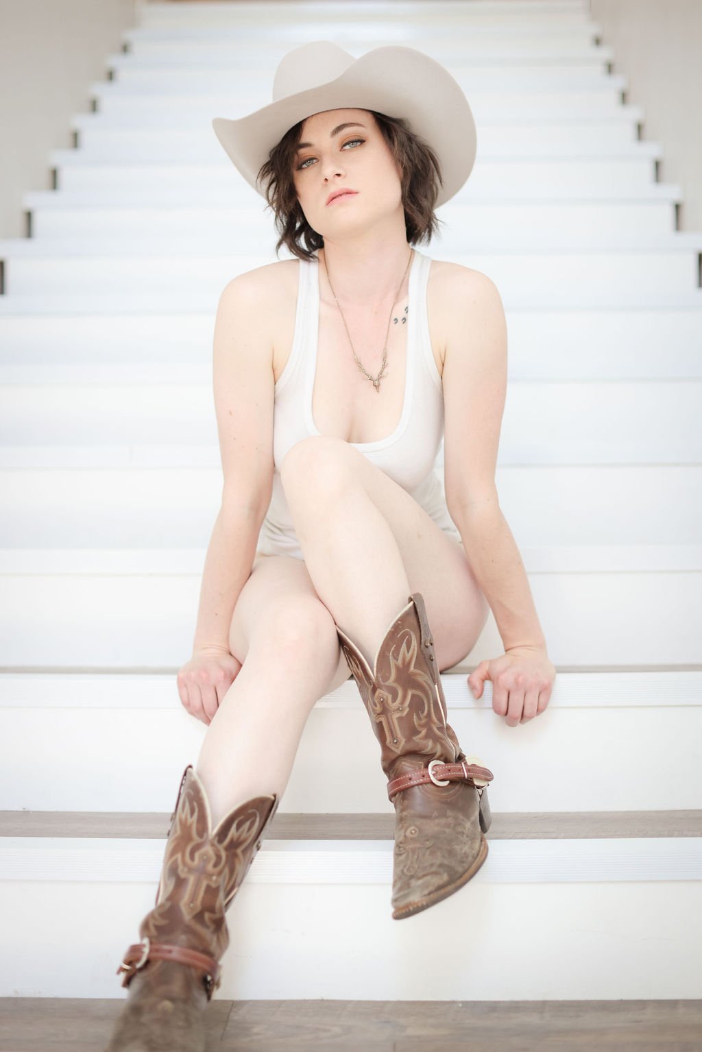 Boudoir session of woman wearing cowboy hat, cowboy boots and sheer white tank.jpg