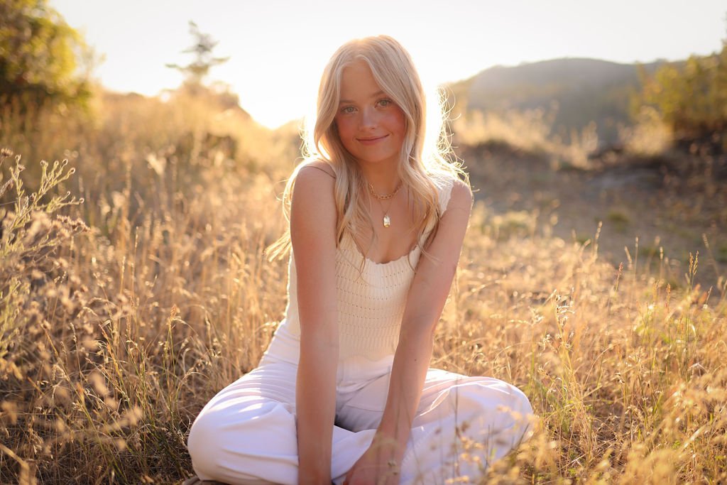 Adorable senior portrait of girl sitting in field at golden hour.jpg