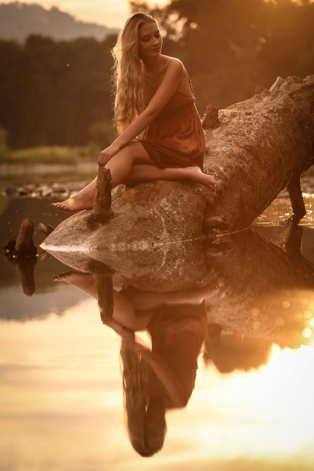 Creative high school senior portrait of girl sitting on log in Montana river at golden hour.jpg