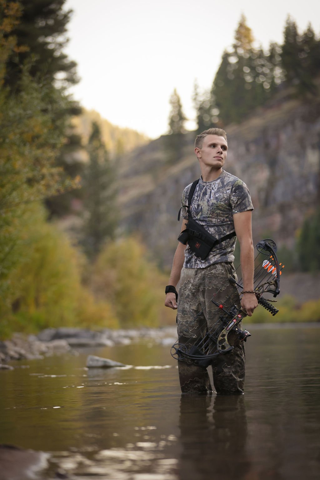 Creative senior portrait ideas of boy in river with bow hunting gear.jpg