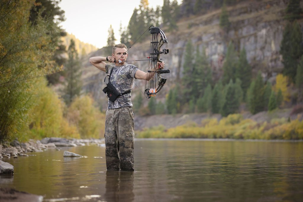 Montana senior portrait of boy standing in river with bow hunting gear.jpg