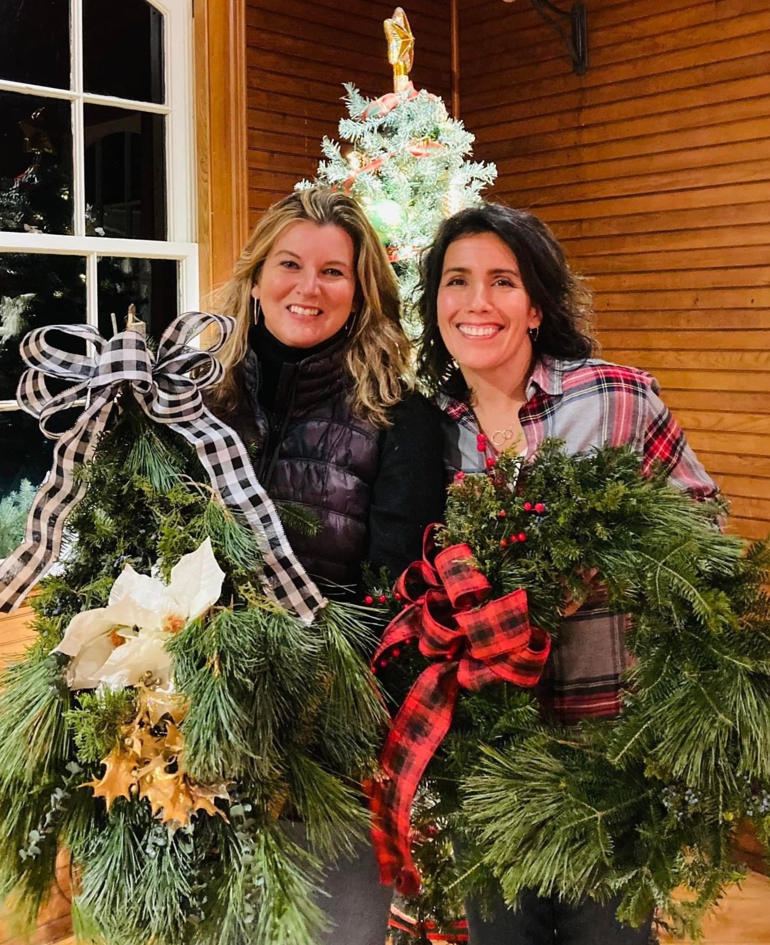 Two women showing their just-made holiday wreaths.