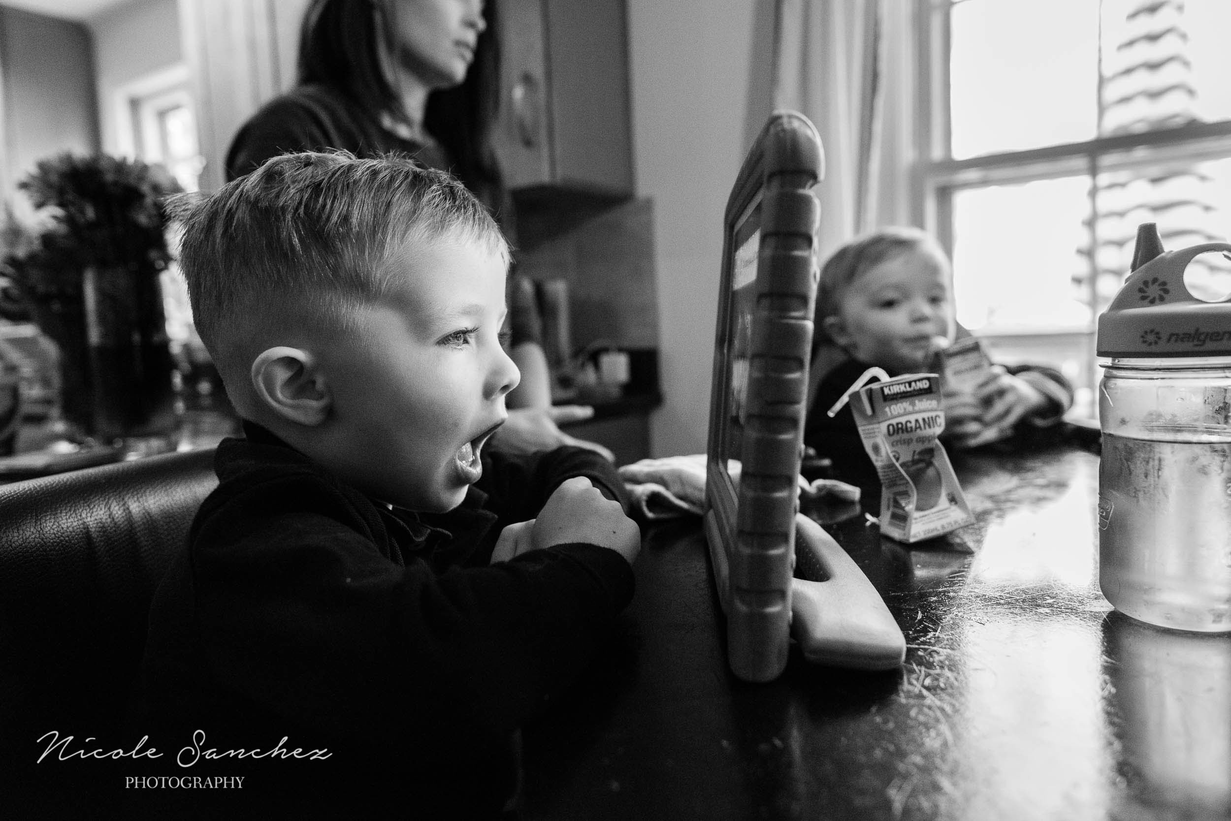 Young boy playing on tablet in kitchen during in-home family photography session by Nicole Sanchez