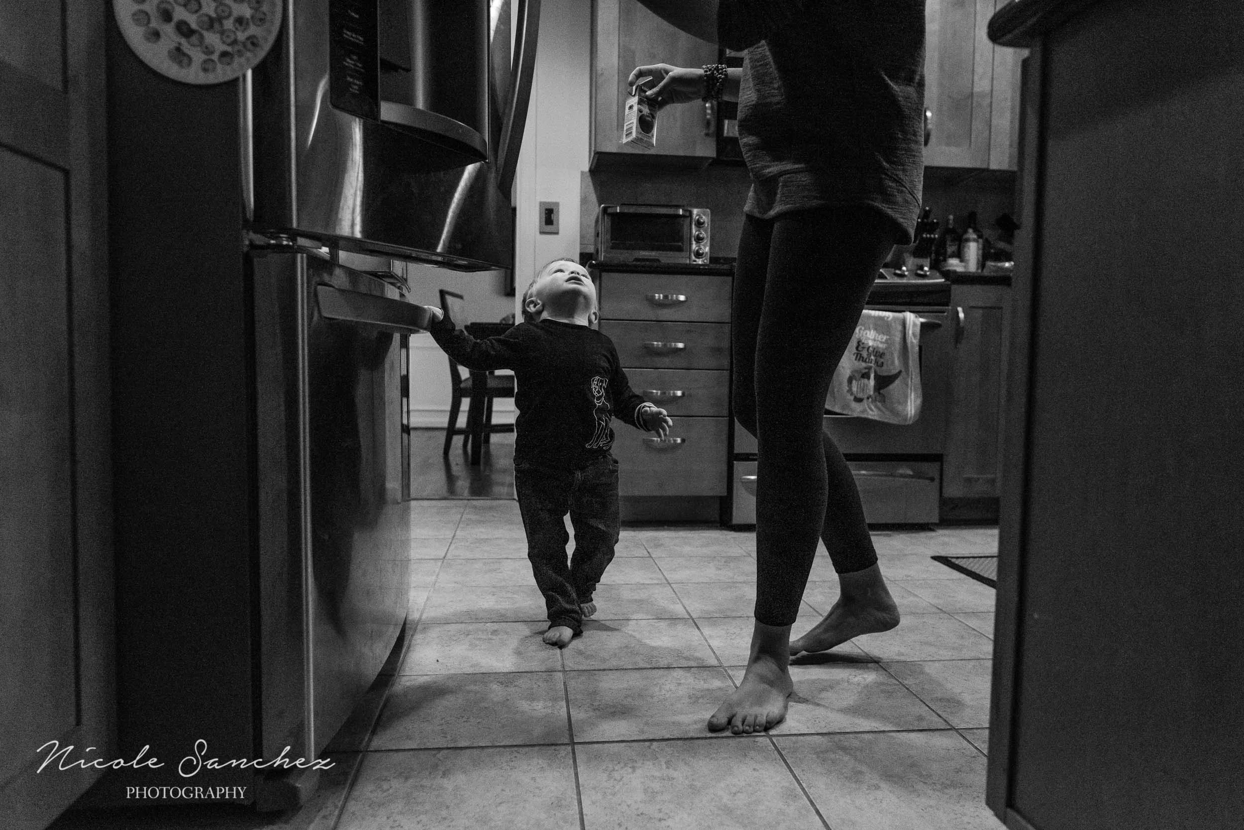 Toddler waiting for mom to give him juice in kitchen at in-home photography session by Documentary Family Photographer Nicole Sanchez