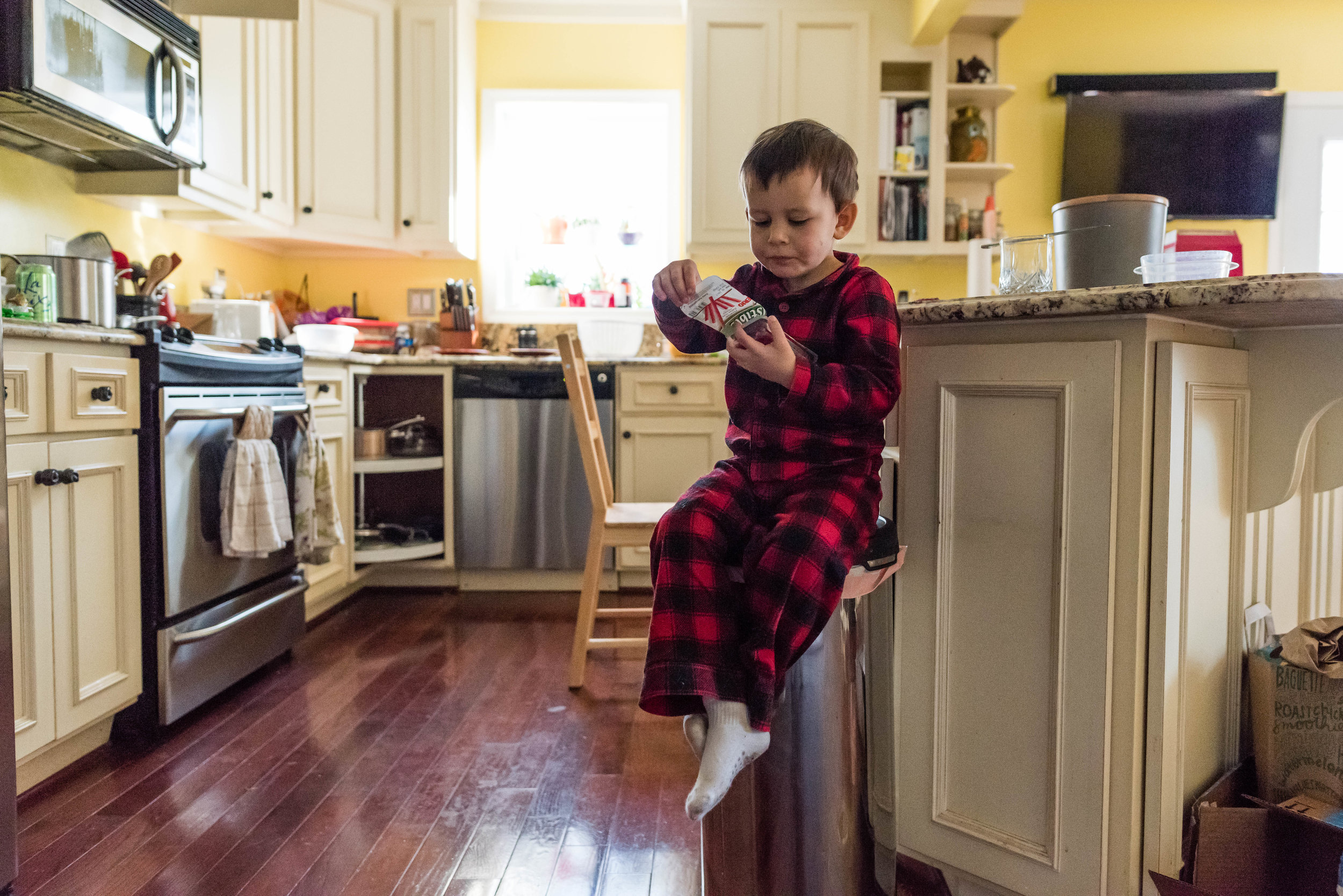 Boy eating yogurt on kitchen trash can in Northern Virginia by Nicole Sanchez Photographer