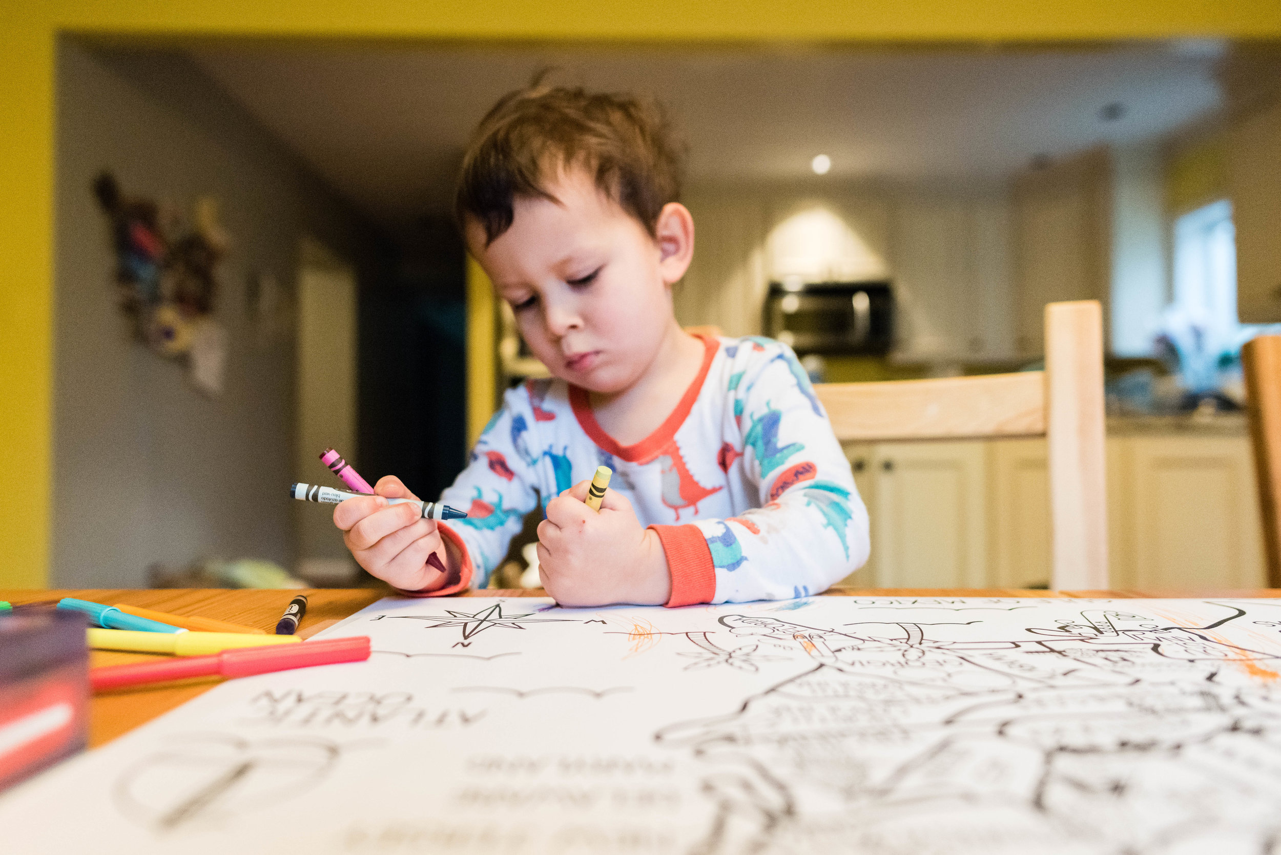 Boy coloring at kitchen table in pajamas by Nicole Sanchez Family Photographer