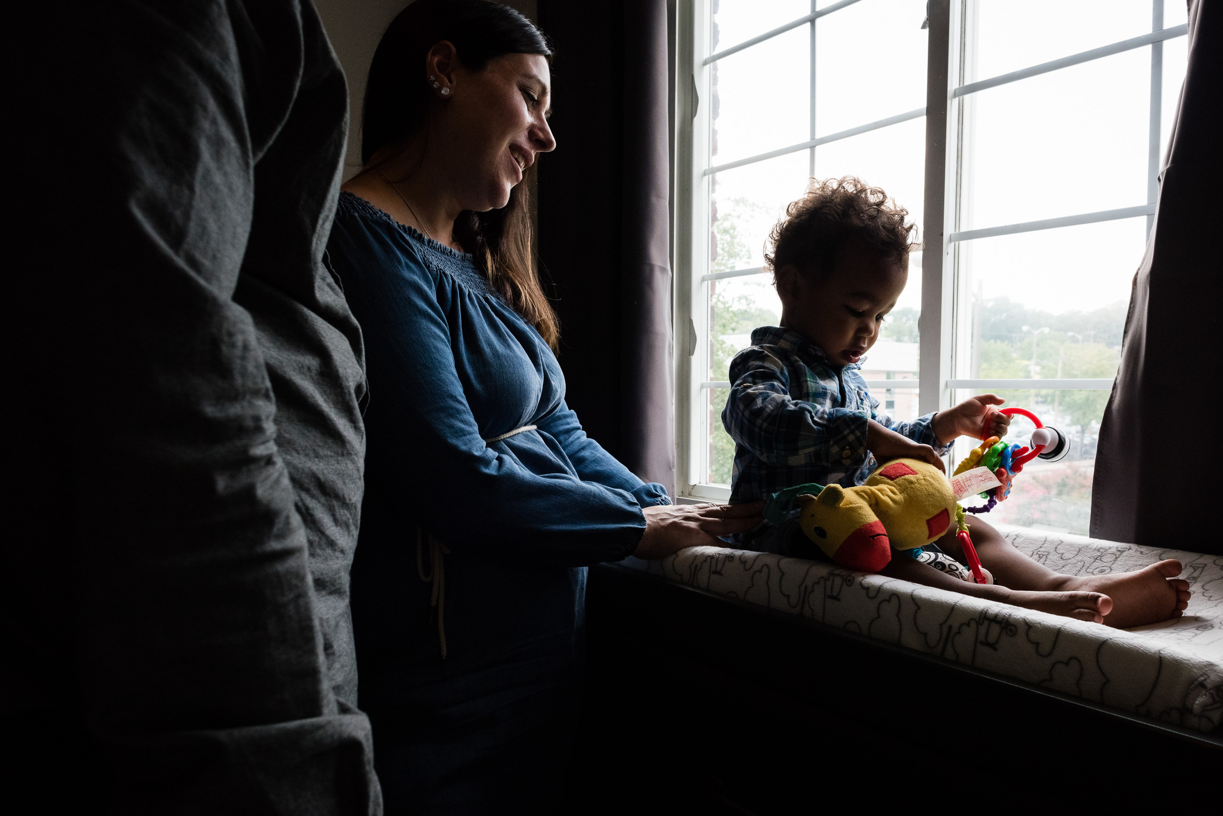 mom and dad playing with son in window at home session in alexandria va by family photographer nicole sanchez