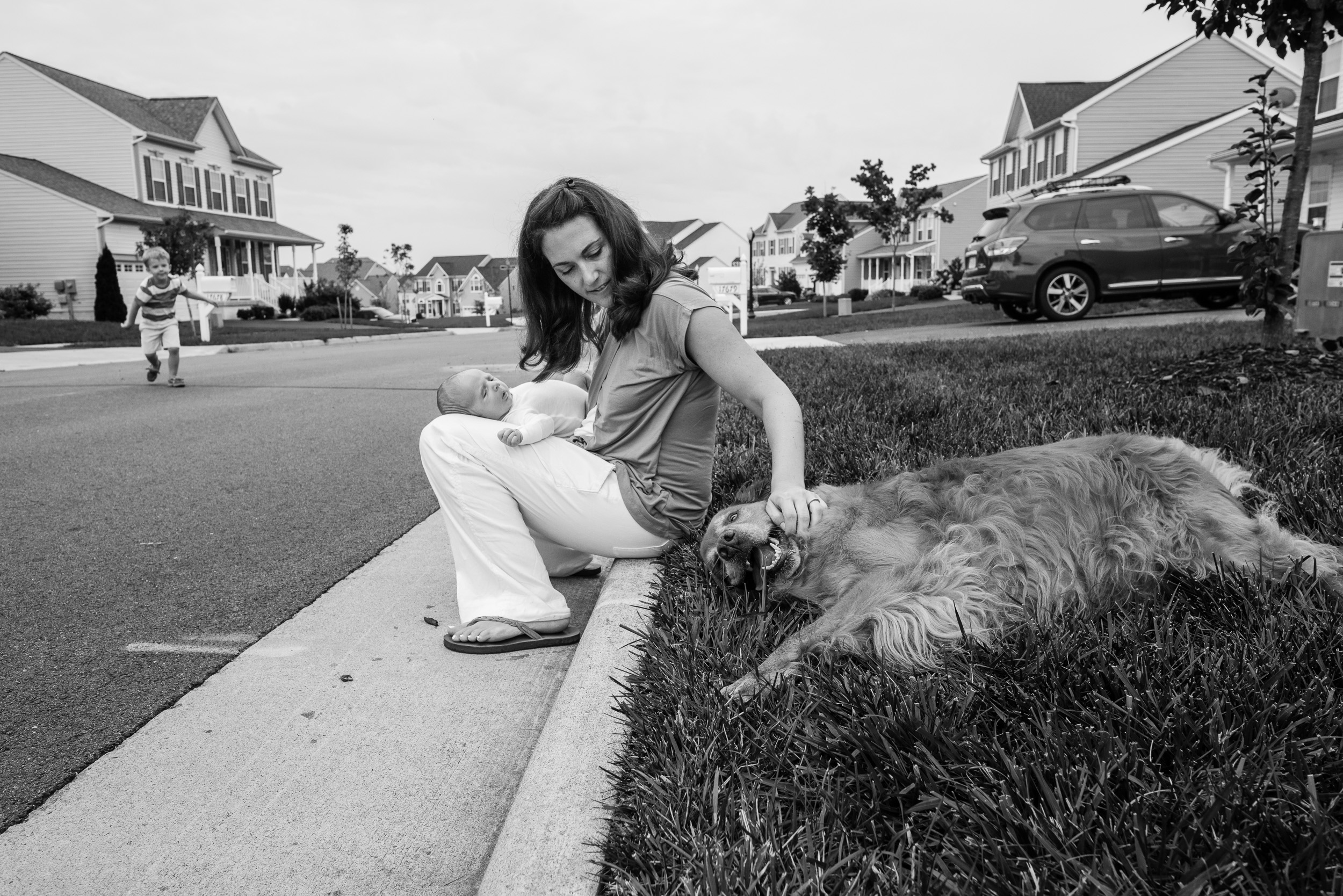 Mom holding newborn baby and petting dog in Northern Virginia neighborhood by Family Photographer Nicole Sanchez