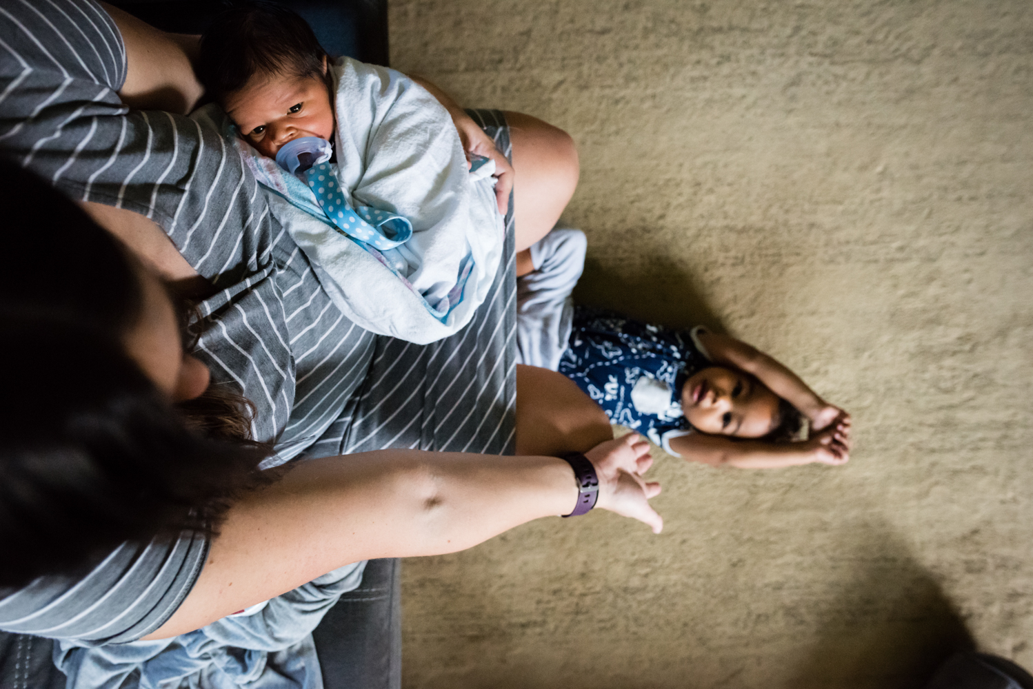 Mom holding newborn while holding hand with son on floor