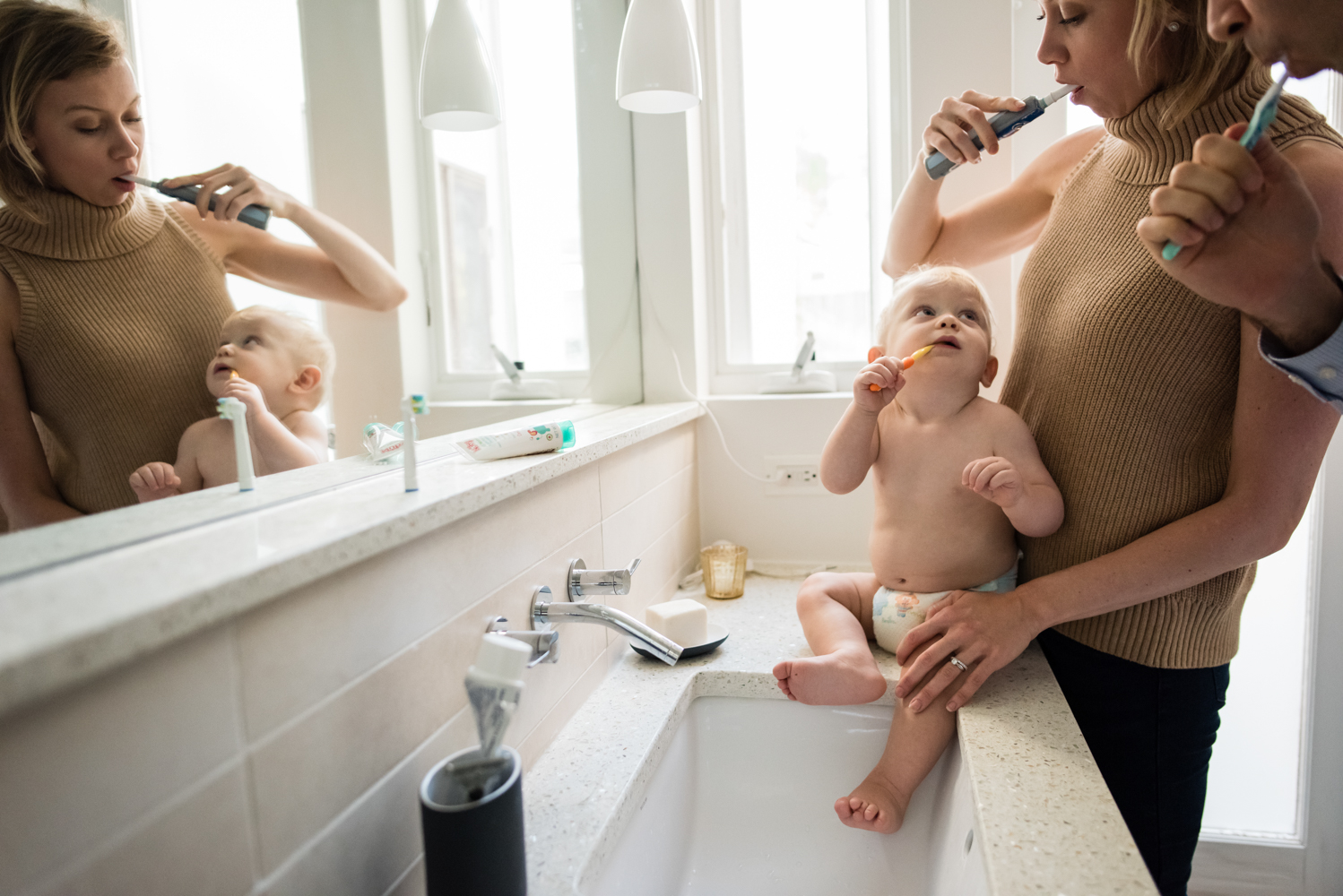 Baby brushing teeth with parents in bathroom