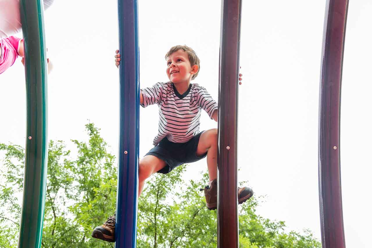 Boy climbing rainbow bars at Clemyjontri playground by Northern Virginia Family Photographer Nicole Sanchez