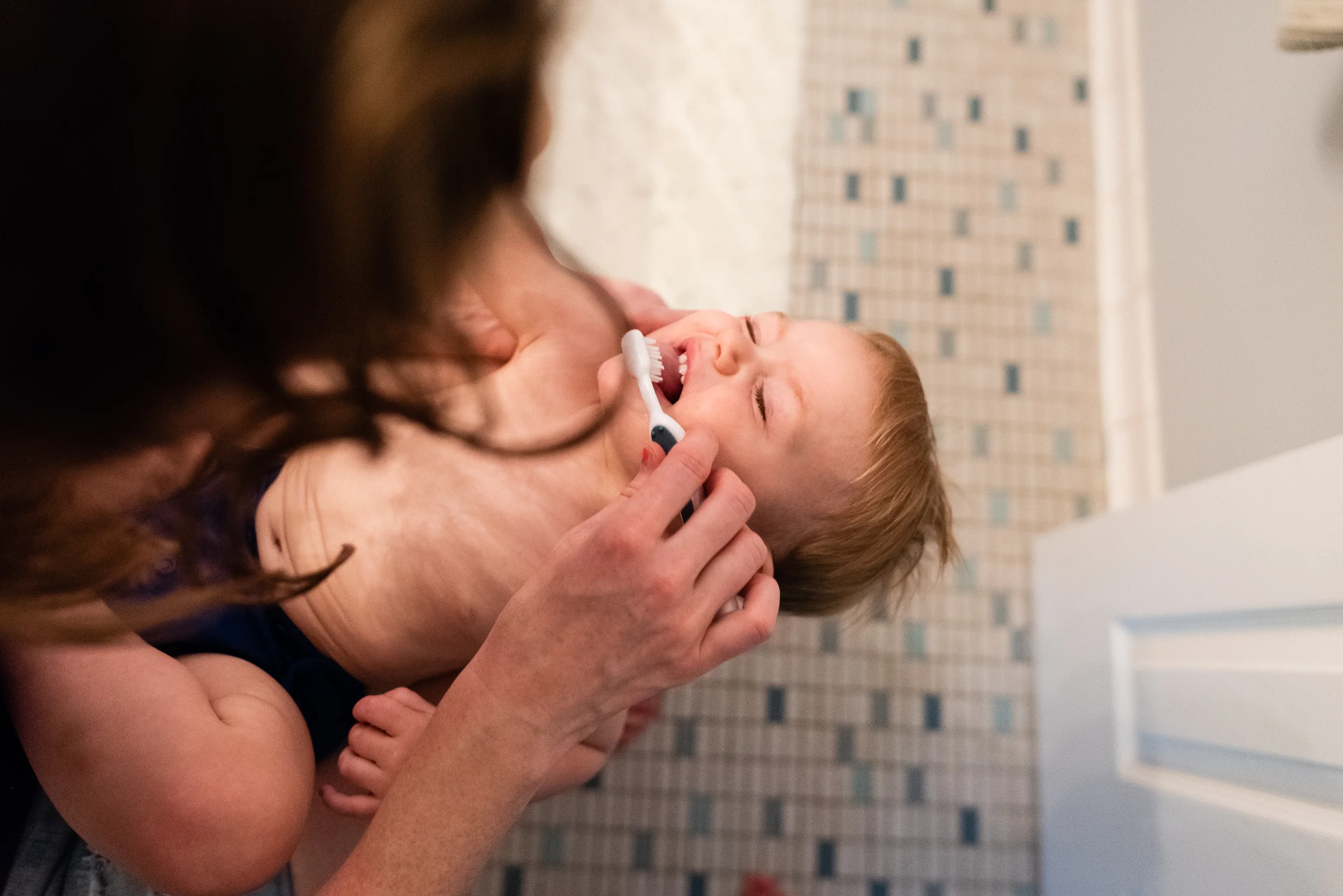 Mom trying to brush toddler's teeth by Northern Virginia Family Photographer Nicole Sanchez