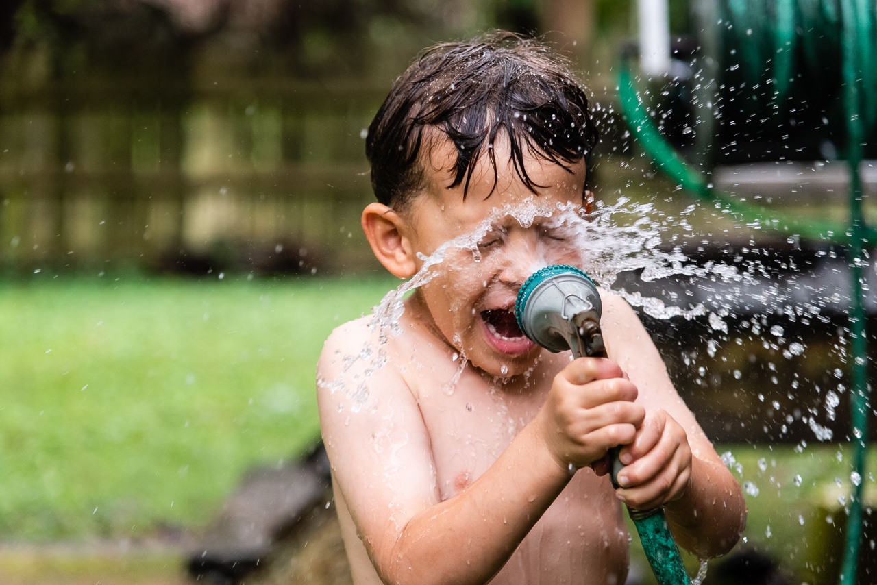 Boy spraying himself in face with waterhose by Northern Virginia Family Photographer Nicole Sanchez