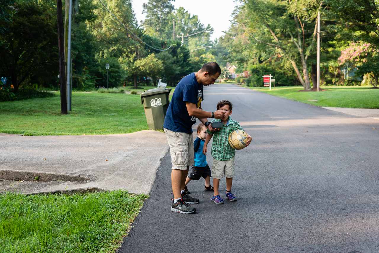 Dad feeding son while walking to school bus stop by Northern Virginia Family Photographer Nicole Sanchez