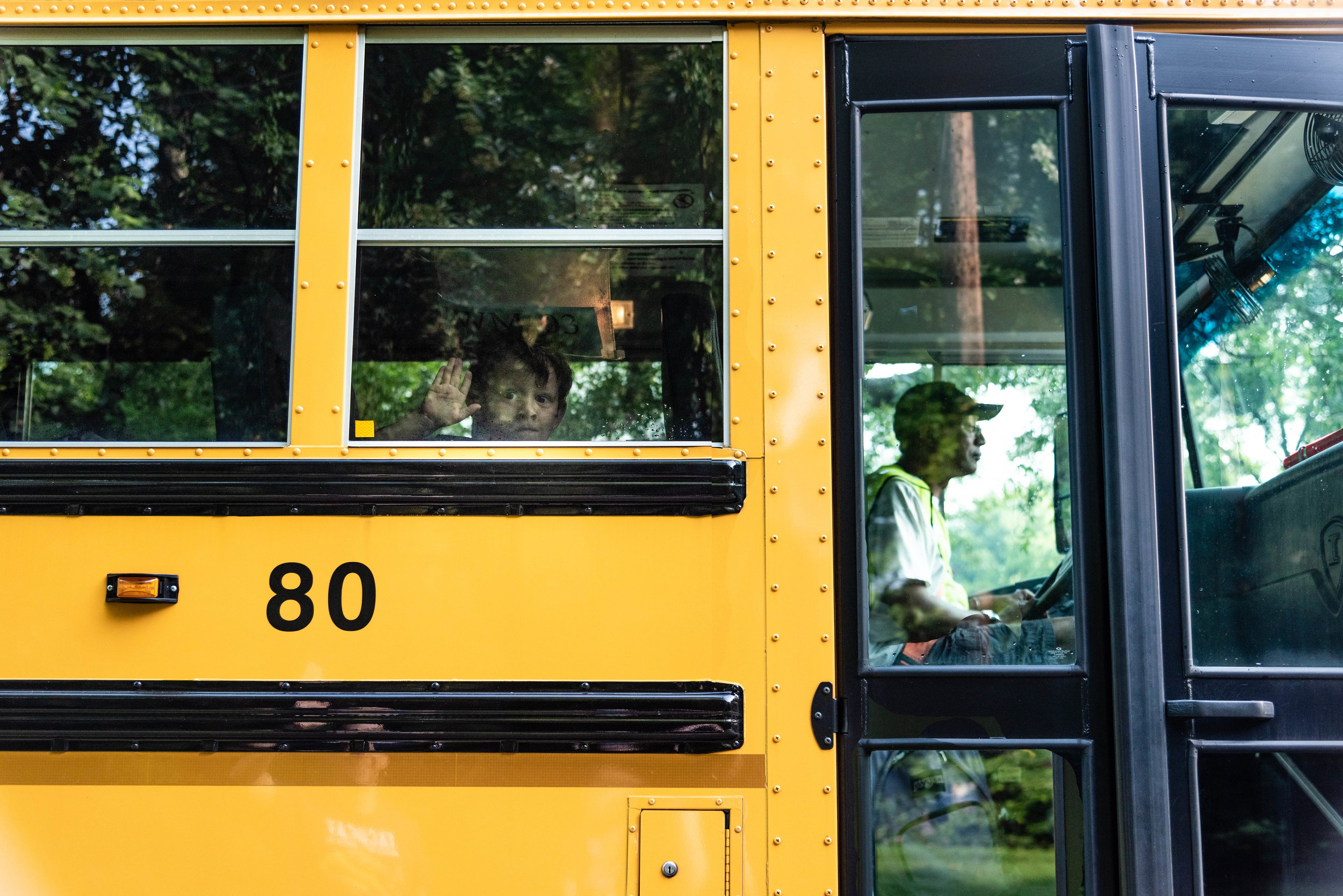 Kindergarten boy waving to family from school bus window in Northern Virginia by Family Photographer Nicole Sanchez