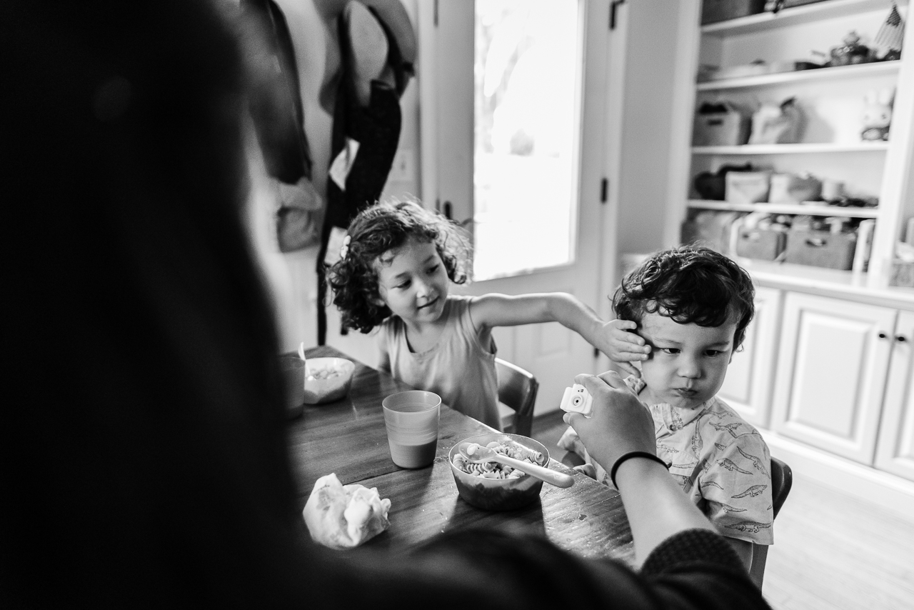 Young girl wiping little brother's face at kitchen table by Northern Virginia Family Photographer Nicole Sanchez