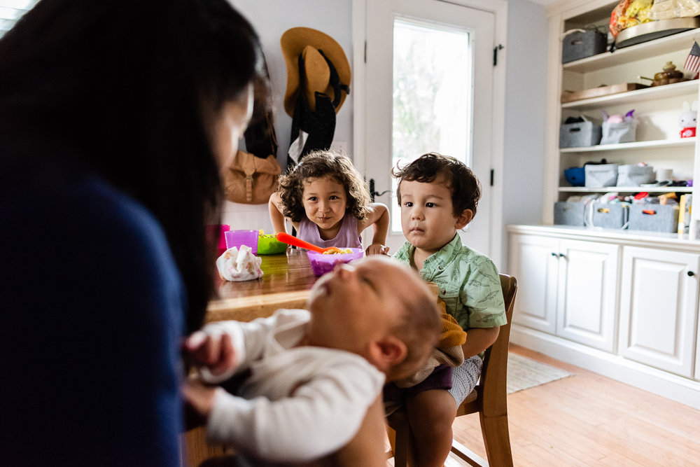 Mom with newborn and siblings having a snack at kitchen table by Northern Virginia Family Photographer Nicole Sanchez