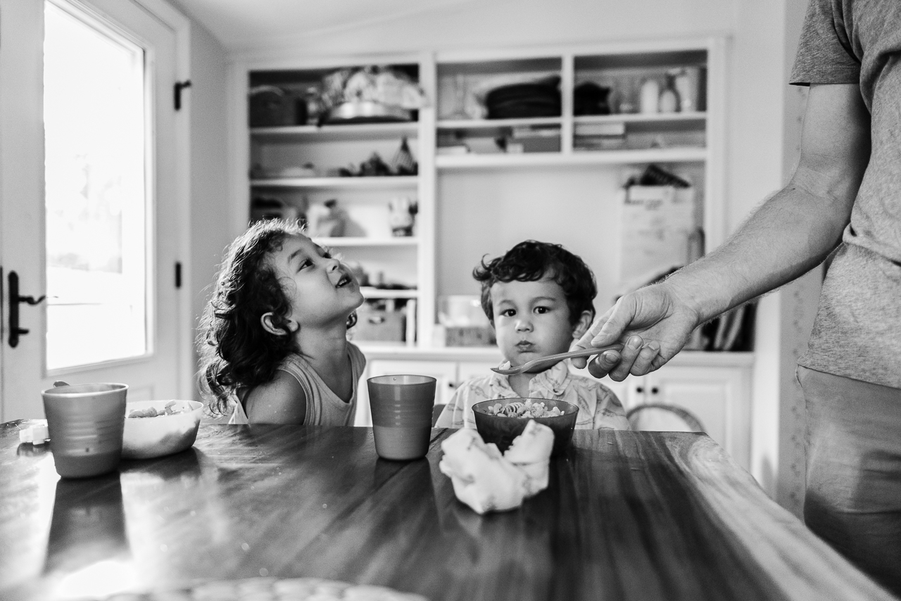 Father trying to feed toddler boy at kitchen table by Northern Virginia Family Photographer Nicole Sanchez