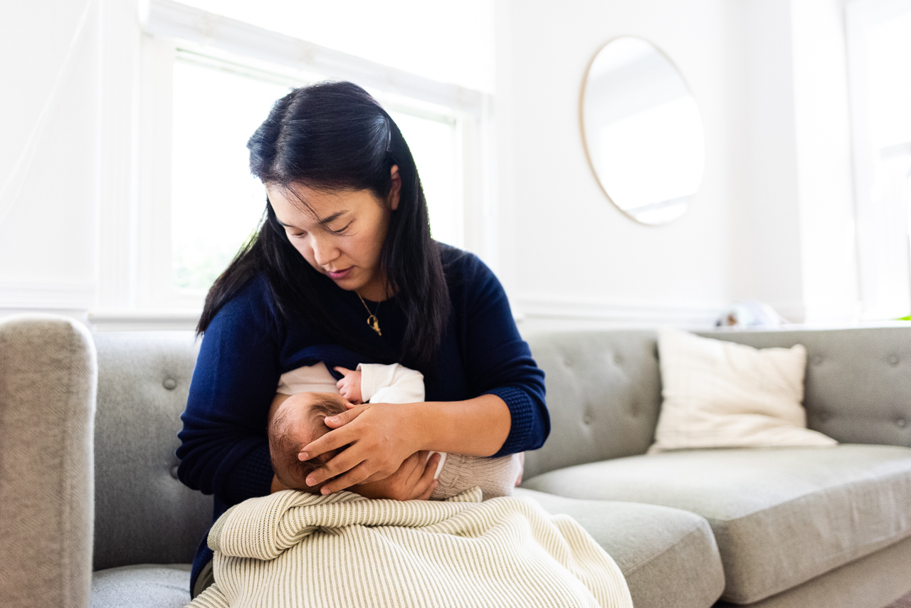 Mother nursing newborn on living room couch by Northern Virginia Family Photographer Nicole Sanchez