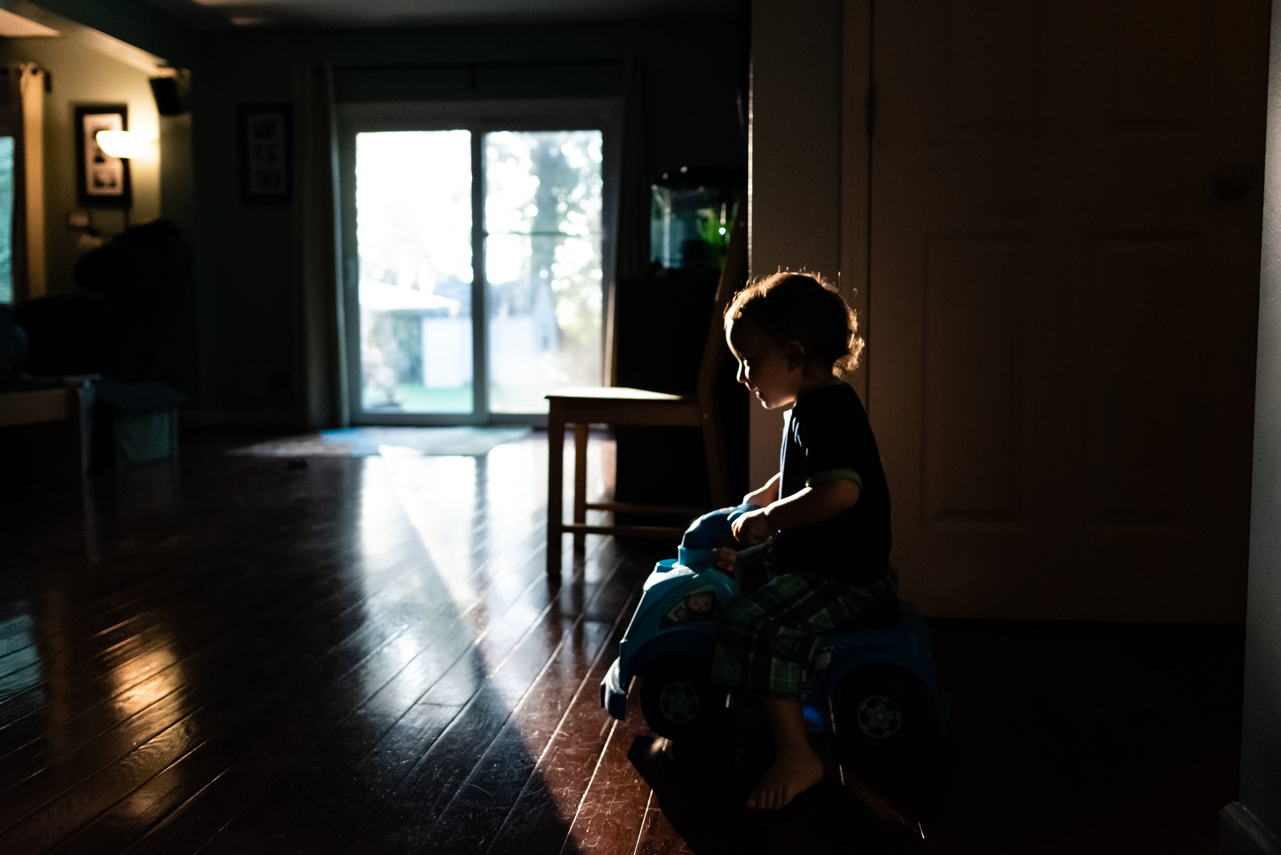 Boy riding car in house in early morning light by Family Photographer Nicole Sanchez