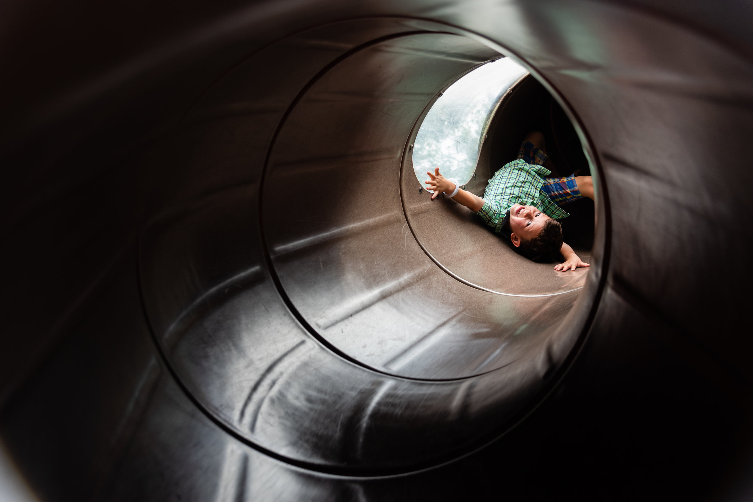 Boy sliding upside down in tunnel slide on playground in Northern Virginia by Family Photographer Nicole Sanchez