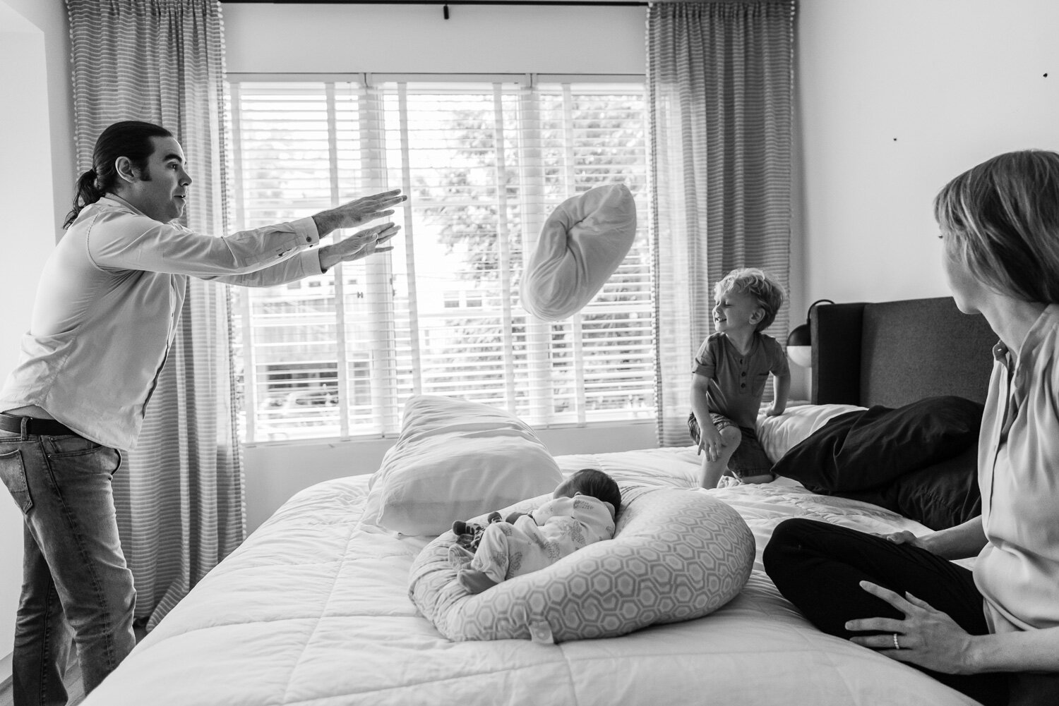 Dad and little boy having a pillow fight with baby sister and mom watching