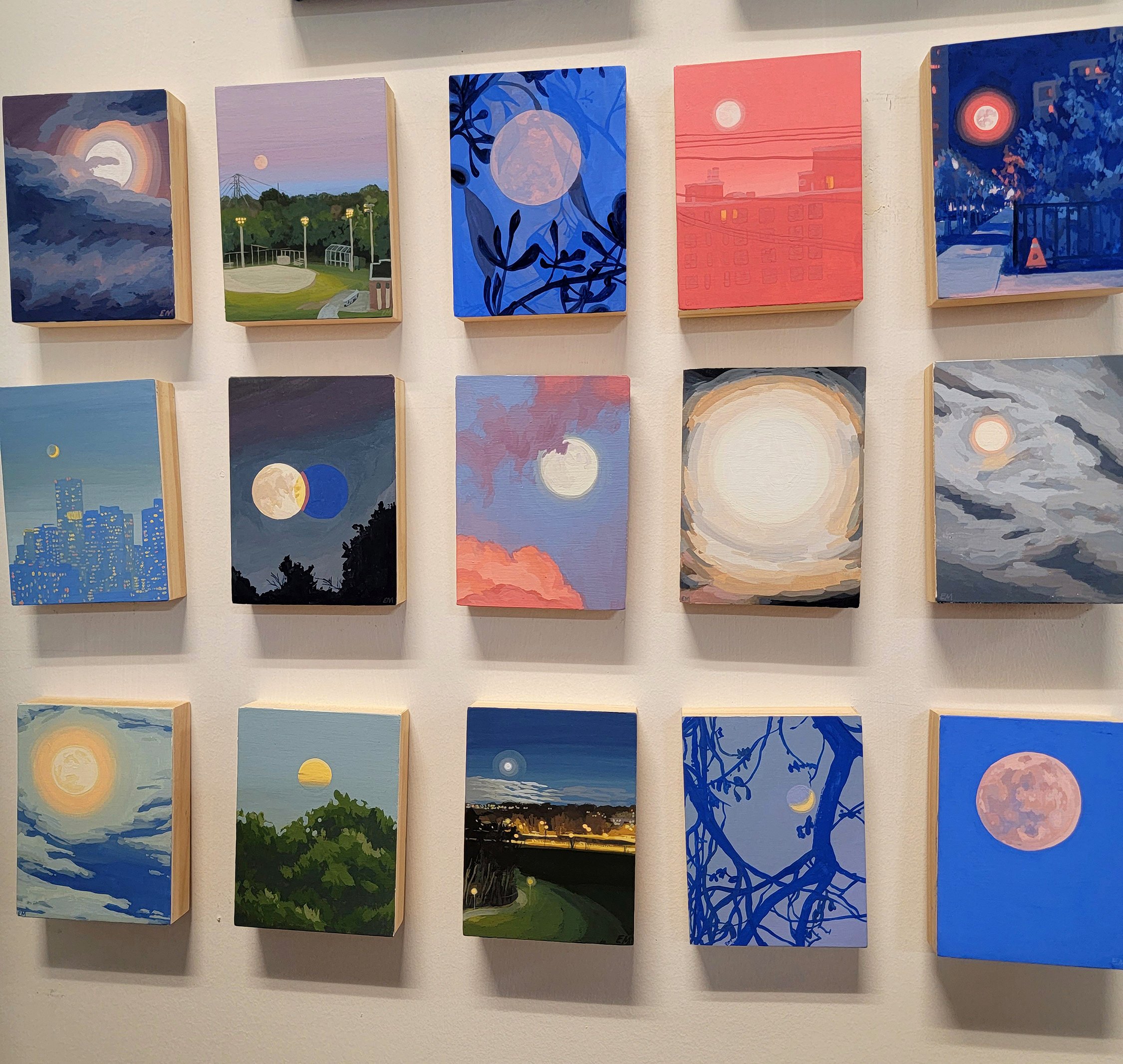   A photograph of 15 small and colourful paintings of moons amidst various backgrounds, including cityscapes, trees and forests, or through thick clouds.&nbsp;  