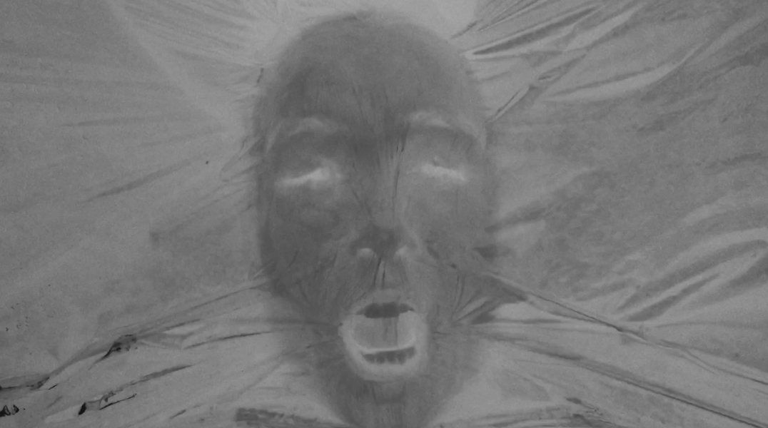   An image of a face pressed into a sheet, the image is in the negative, where lights and darks are reversed. The mouth is open and the eyes are closed.&nbsp;  