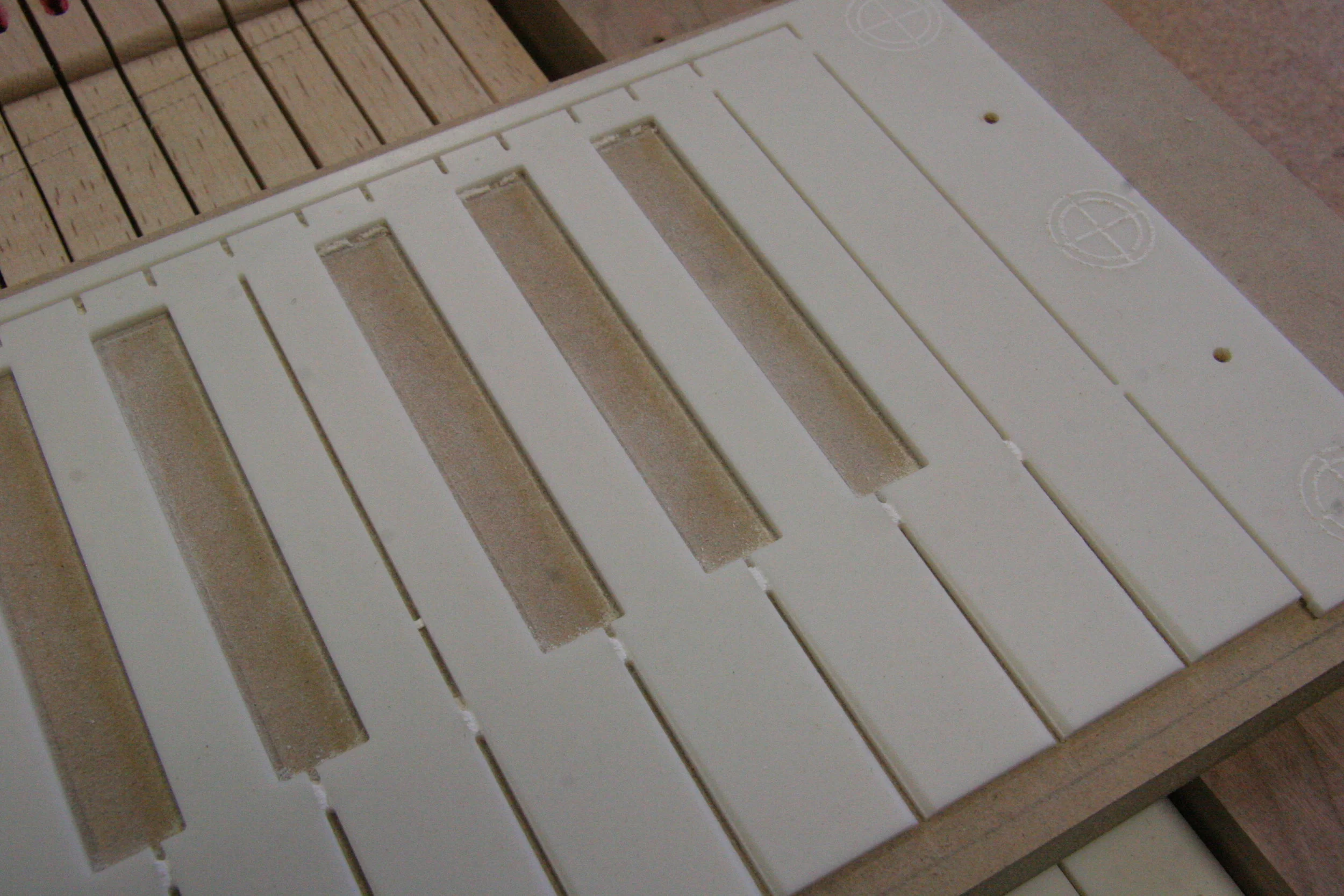 Naturals are machined from solid surface countertop materials. This photo shows blank after CNC machining leaving tabs and registration pin holes behind sharps to aid in placement on keyboard blank.