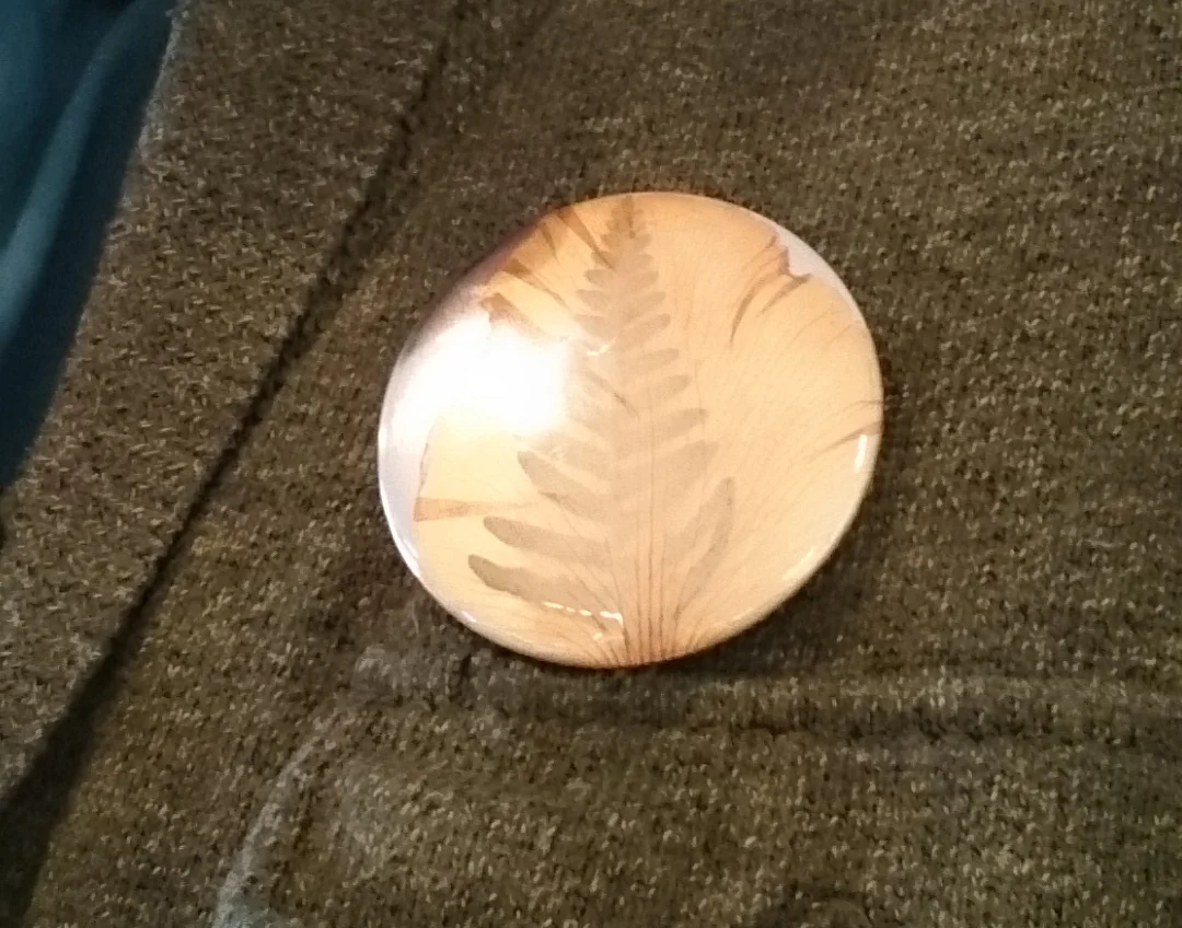 A handmade badge using a fern and translucent petal
