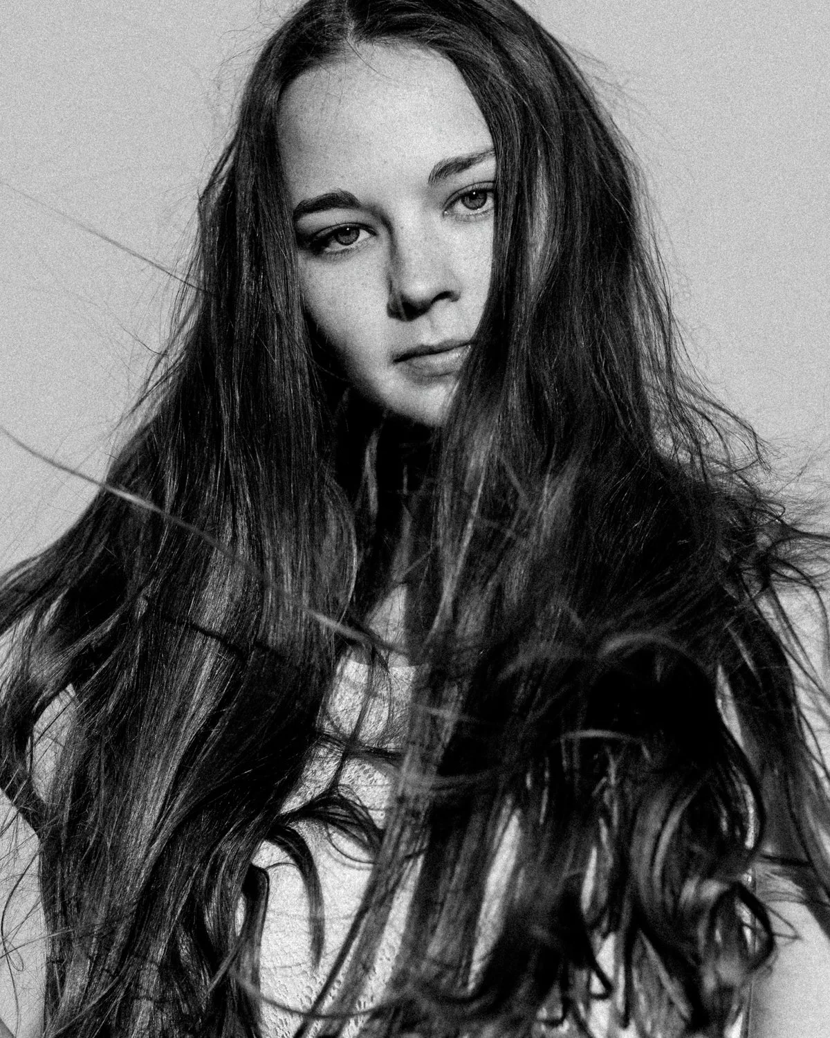 Black and white portrait of a young woman with long, wavy hair, looking at the camera.