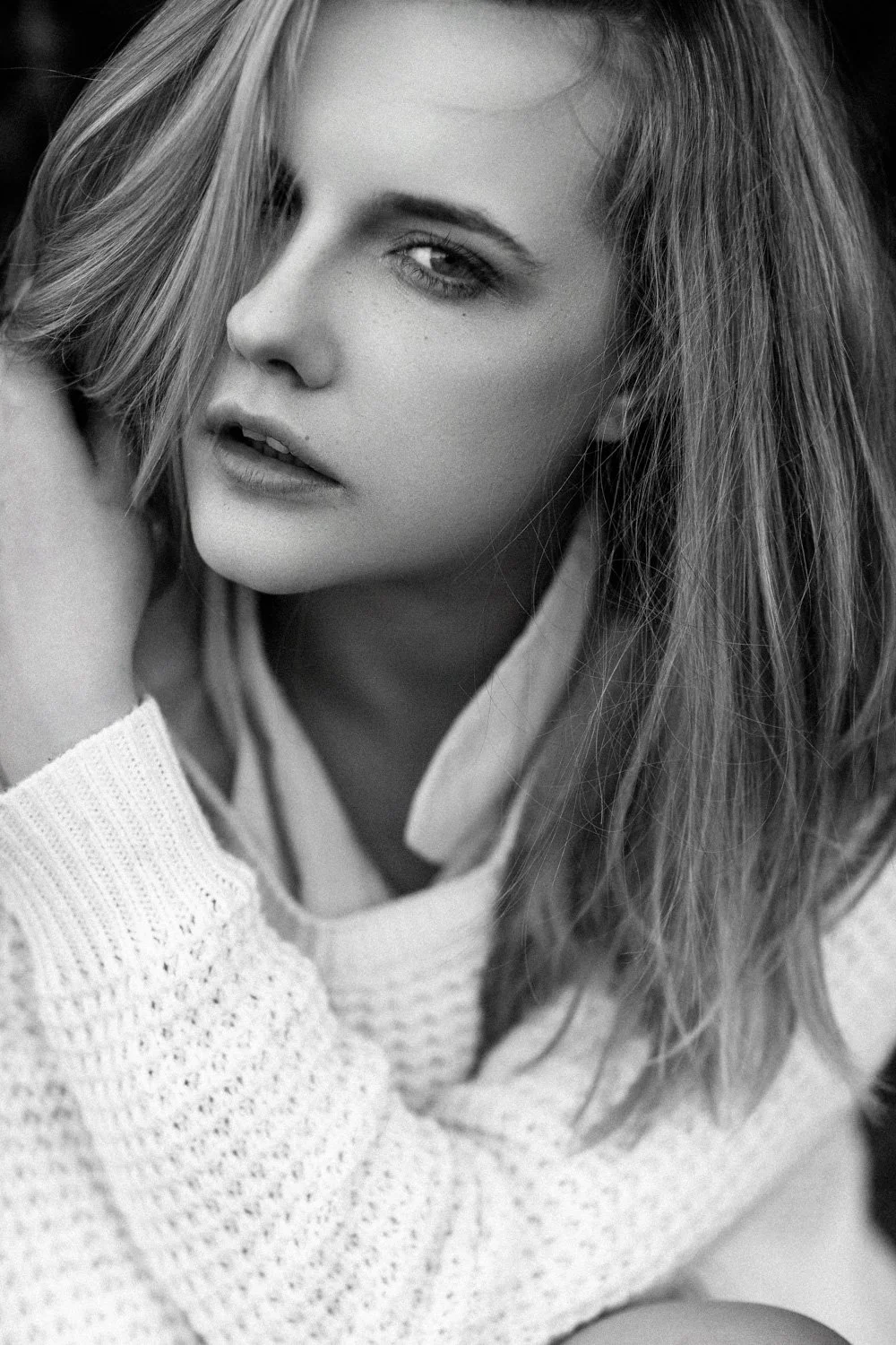 A black and white close-up portrait of a young woman with tousled hair, looking confidently at the camera.
