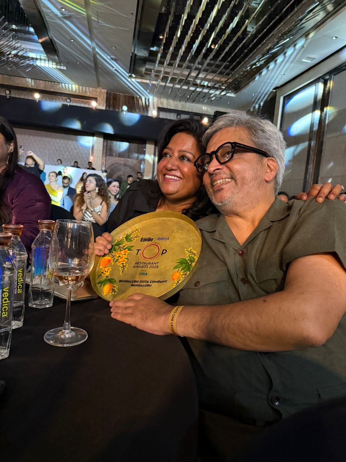 Two people at an award ceremony, smiling and holding a floral decorated plaque that reads 'TOP RESTAURANT AWARDS 2025'.