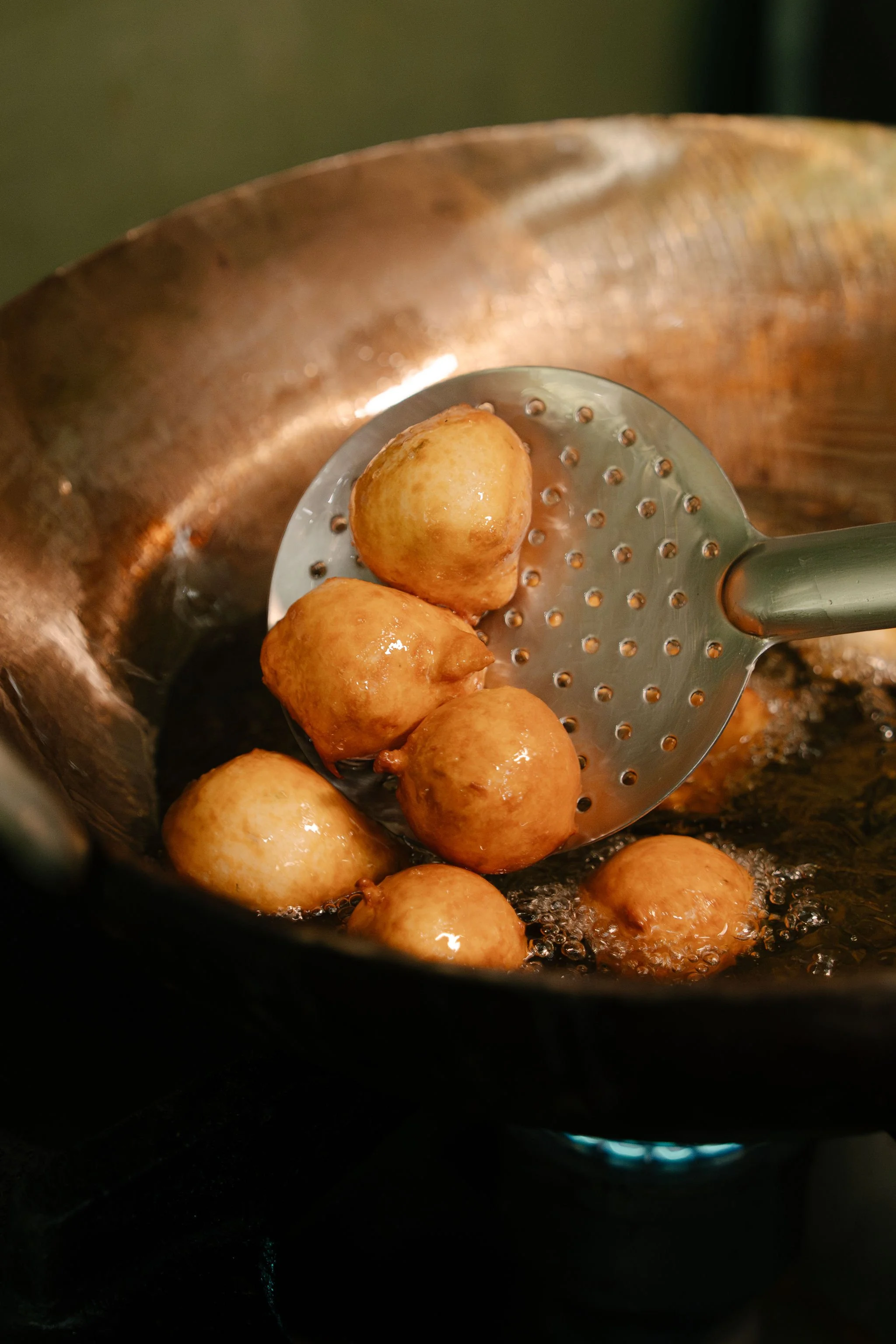 Frying small round pastries or dough balls in a pan with hot oil, using a slotted spatula.